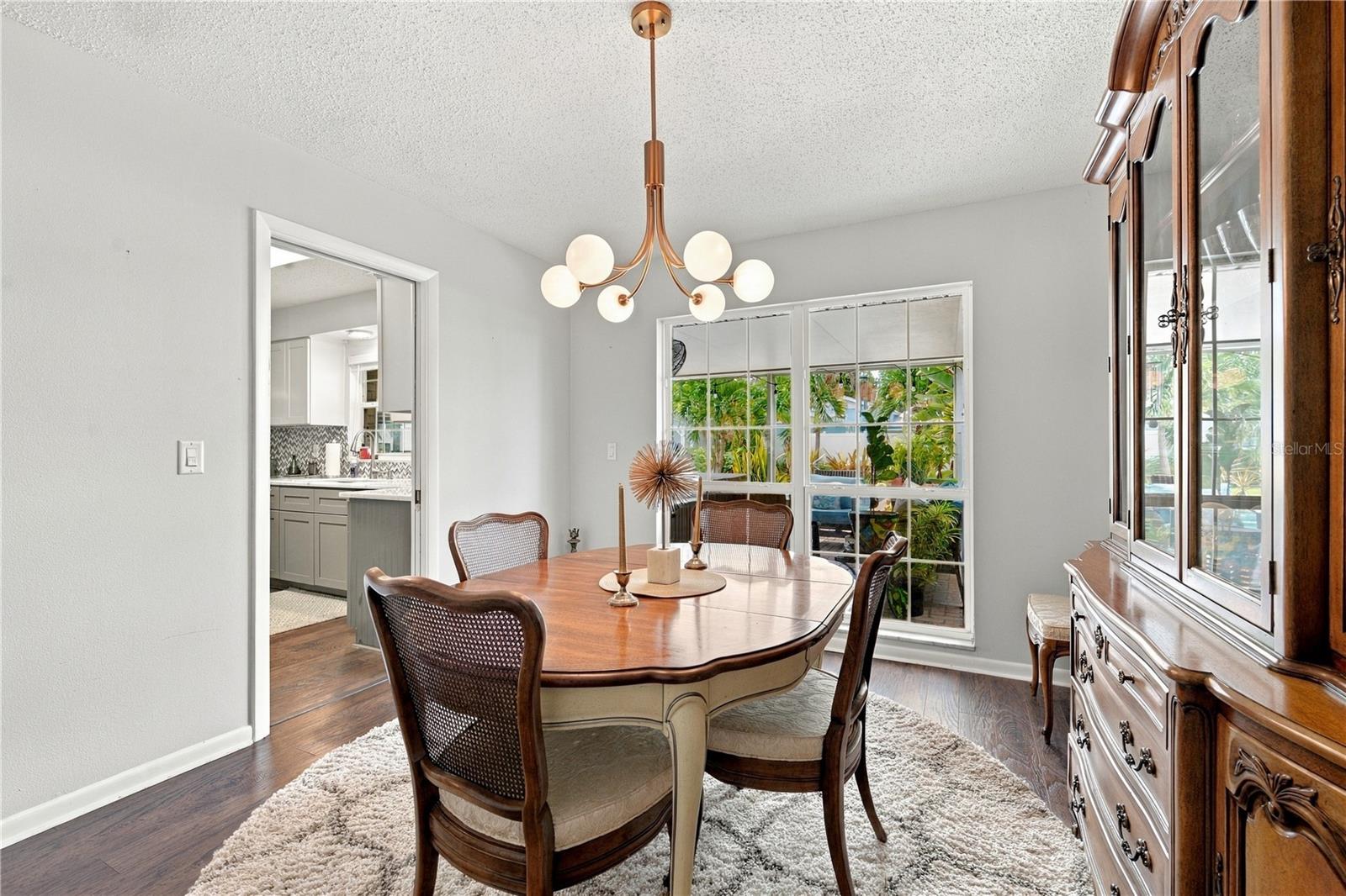 Dining room with a wooden table, globe chandelier, and wide windows overlooking greenery.