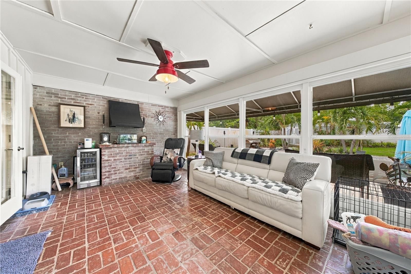Enclosed patio with brick flooring, a brick television wall, and large windows overlooking the yard.