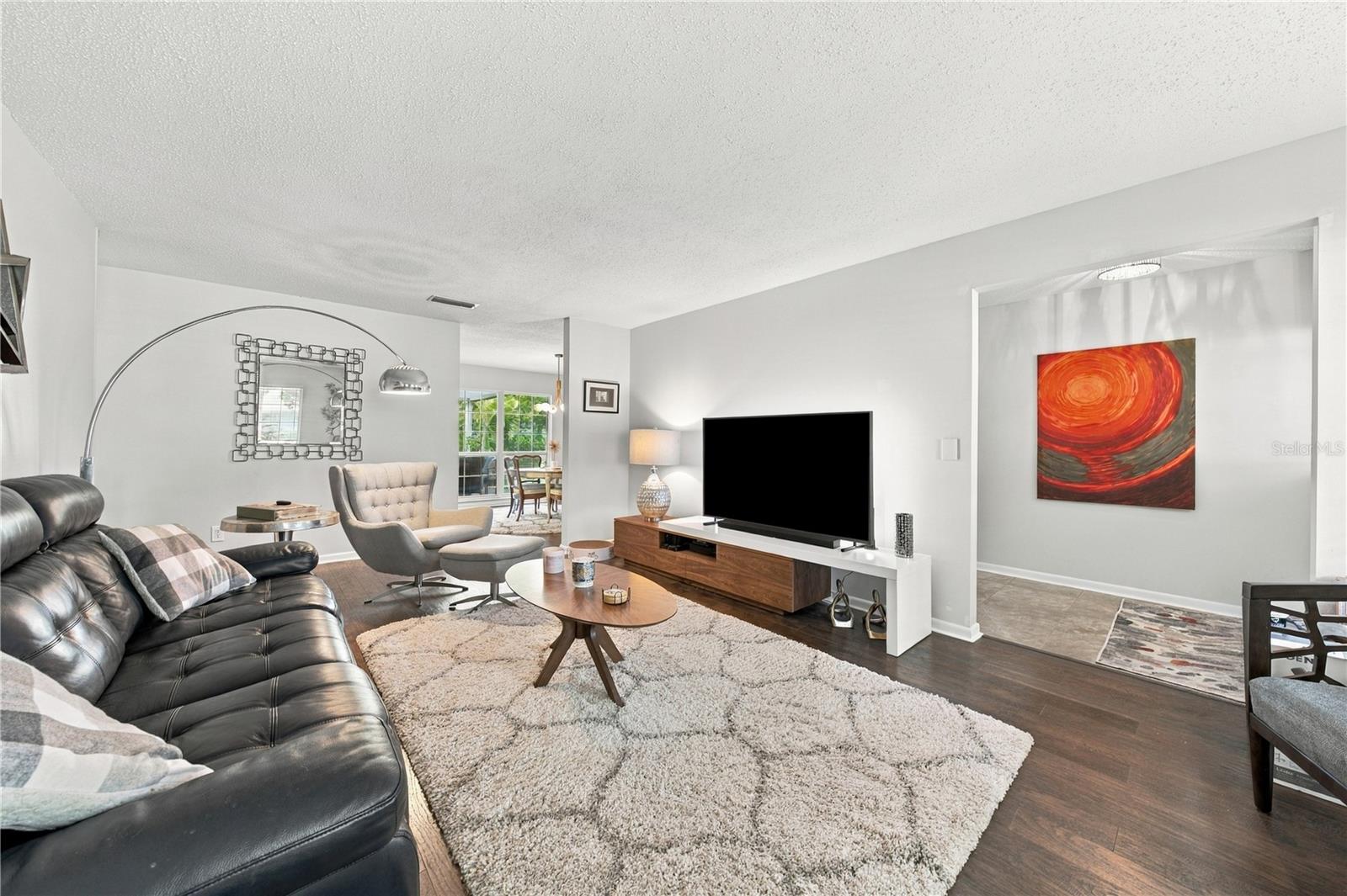 Furnished living room with a black leather sectional, large white rug, and open view to the dining area.