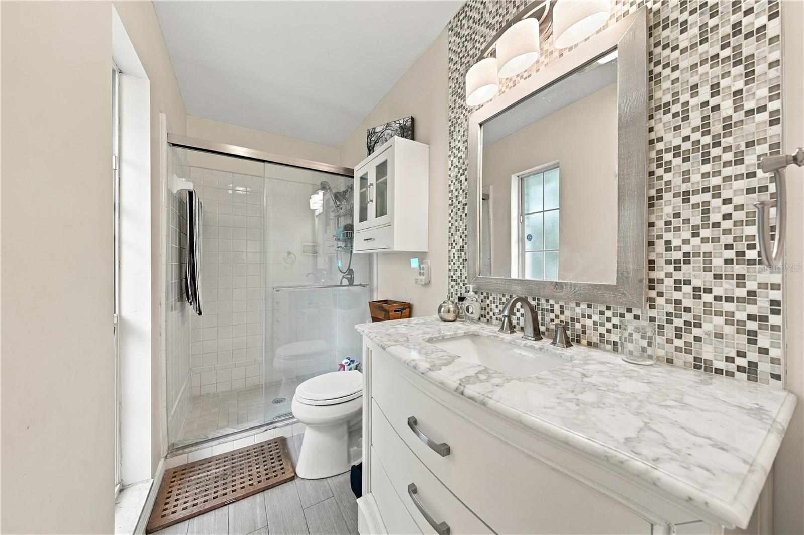 Bathroom with mosaic tile, a marble-look vanity, and a glass-enclosed shower.