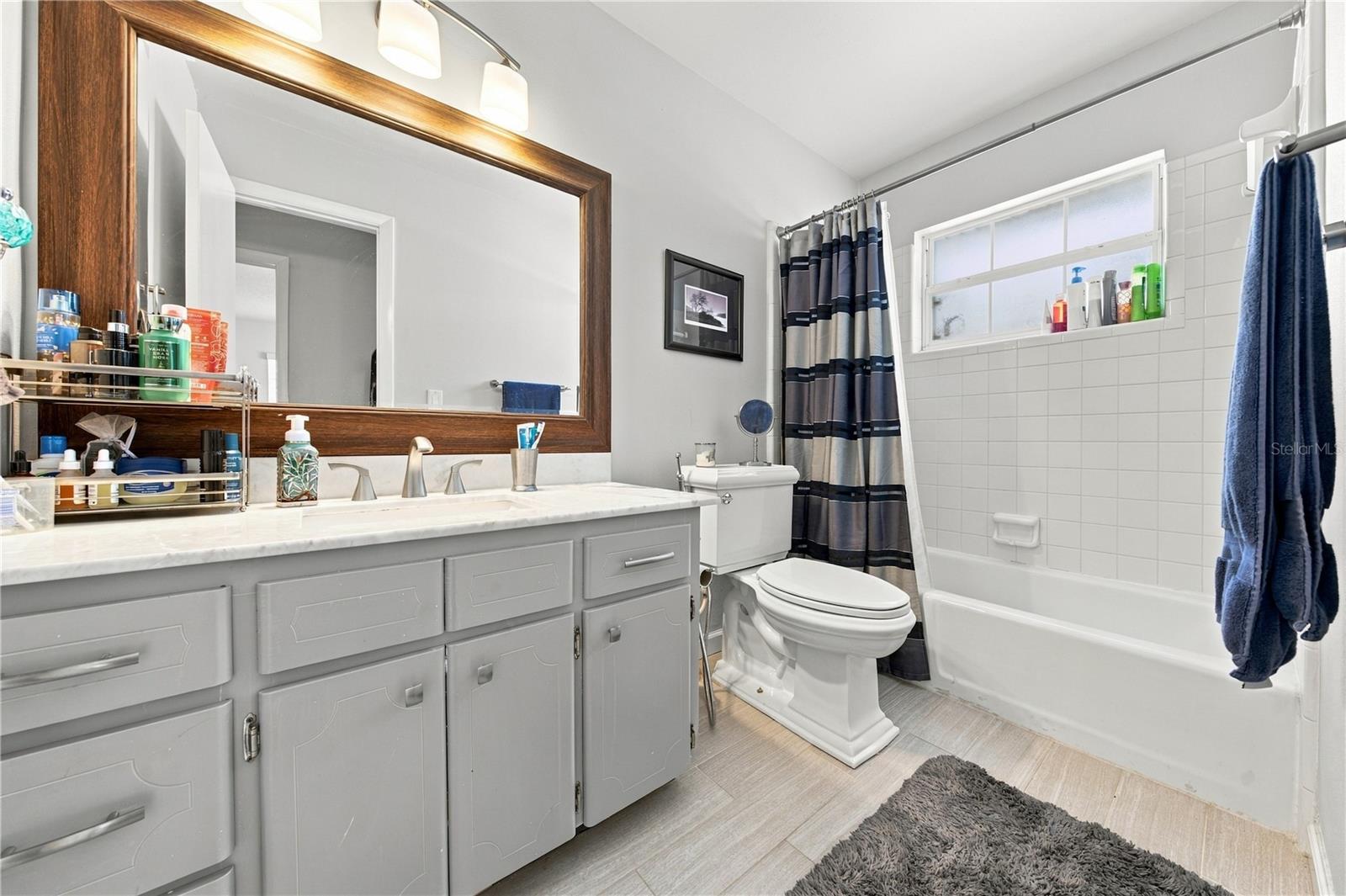 Bathroom with a long gray vanity, wood-framed mirror, and white tub with striped shower curtain.