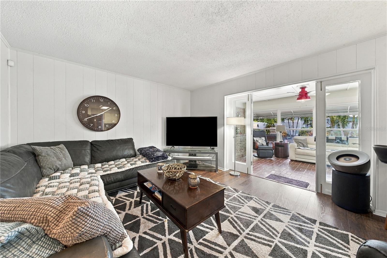 Living room with a dark sectional and glass doors opening to a bright enclosed sunroom.