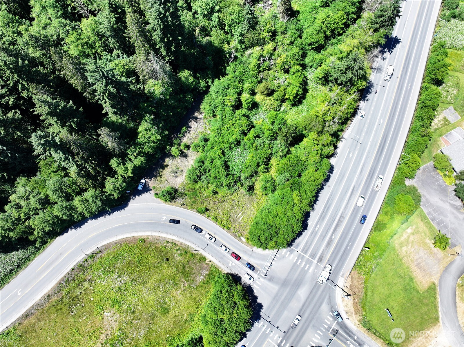 Aerial view of a wooded property beside a busy intersection and curved access road.