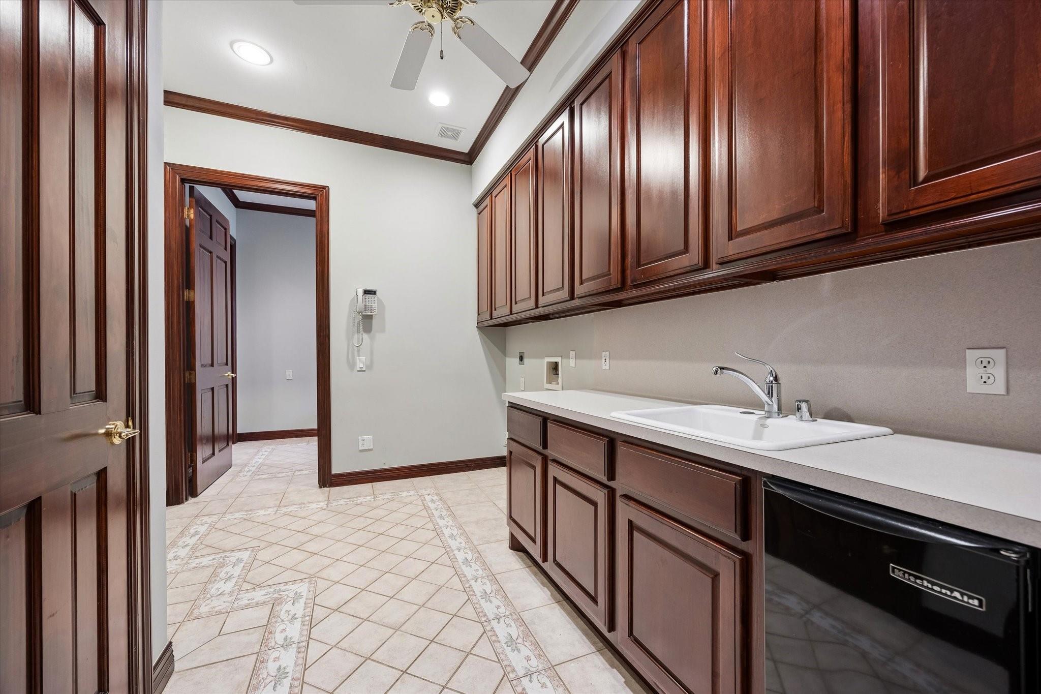 Utility room with dark wood cabinetry, a long white counter and sink, and a black KitchenAid appliance.