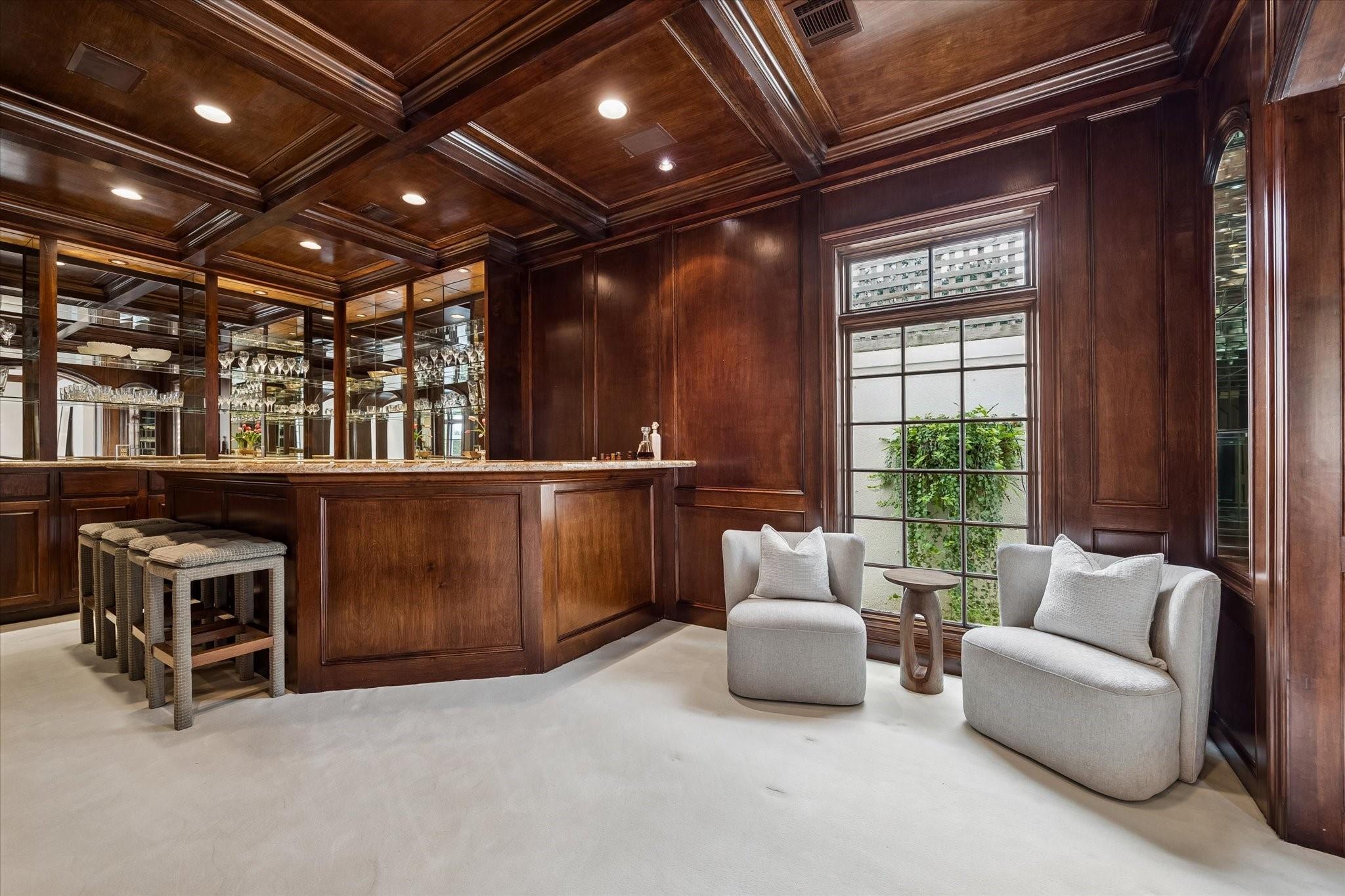 Home bar with mirrored shelving, dark wood paneling, and a window-side seating area.