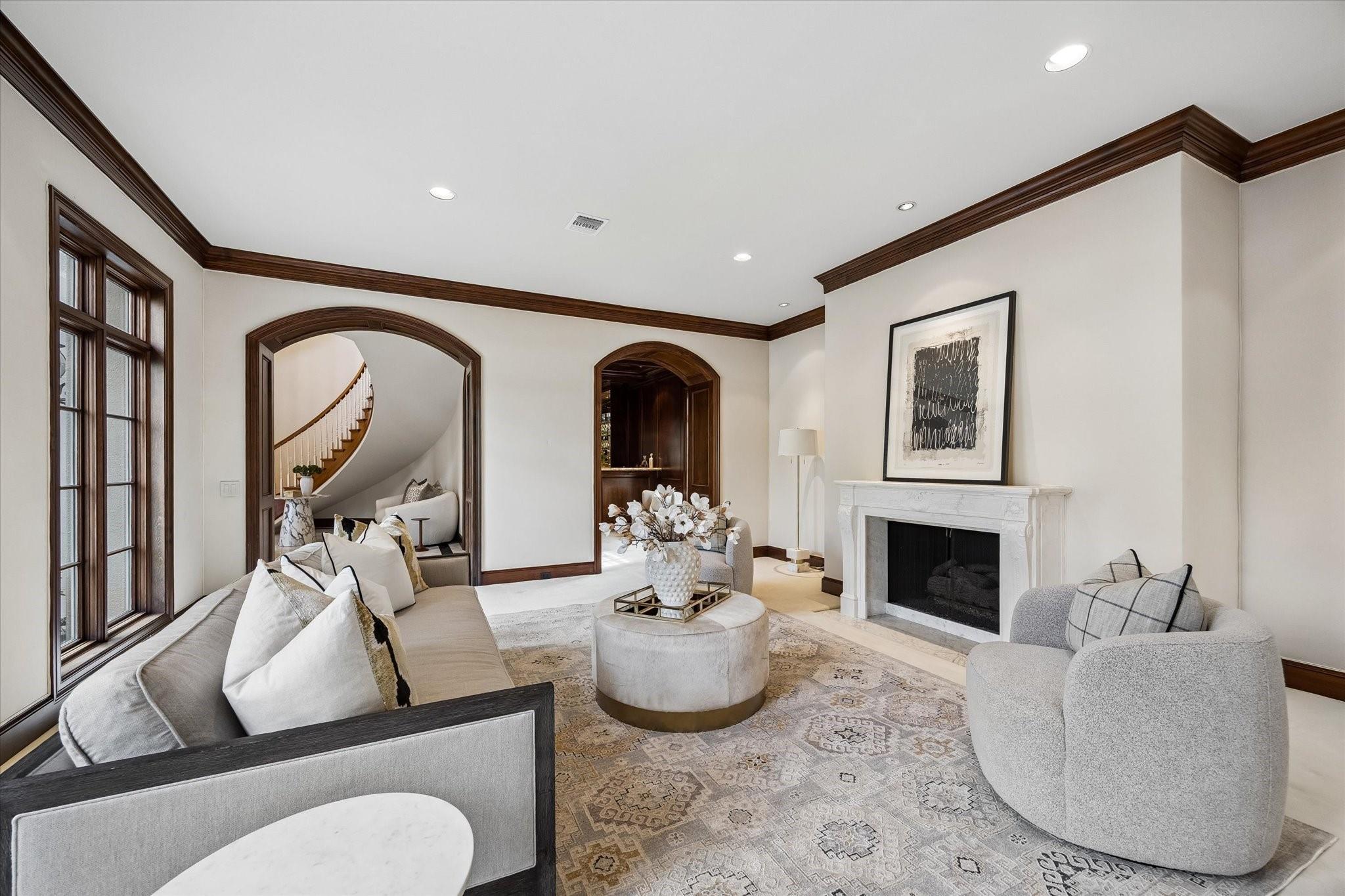 Living room with a white fireplace, arched openings, and a view of a curved staircase.