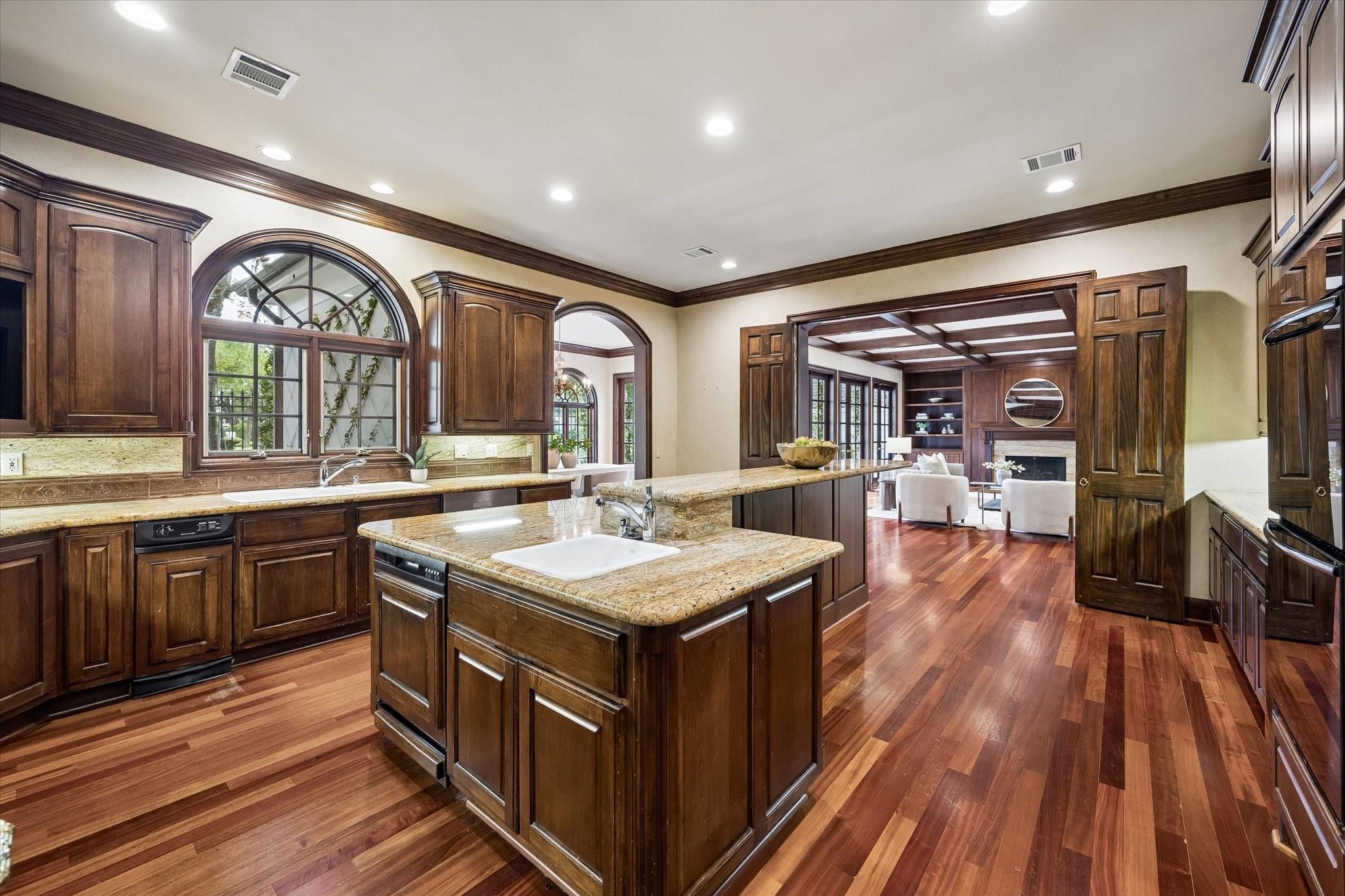 Kitchen with dark wood cabinets, granite island, hardwood floors, and open doors to a living room.
