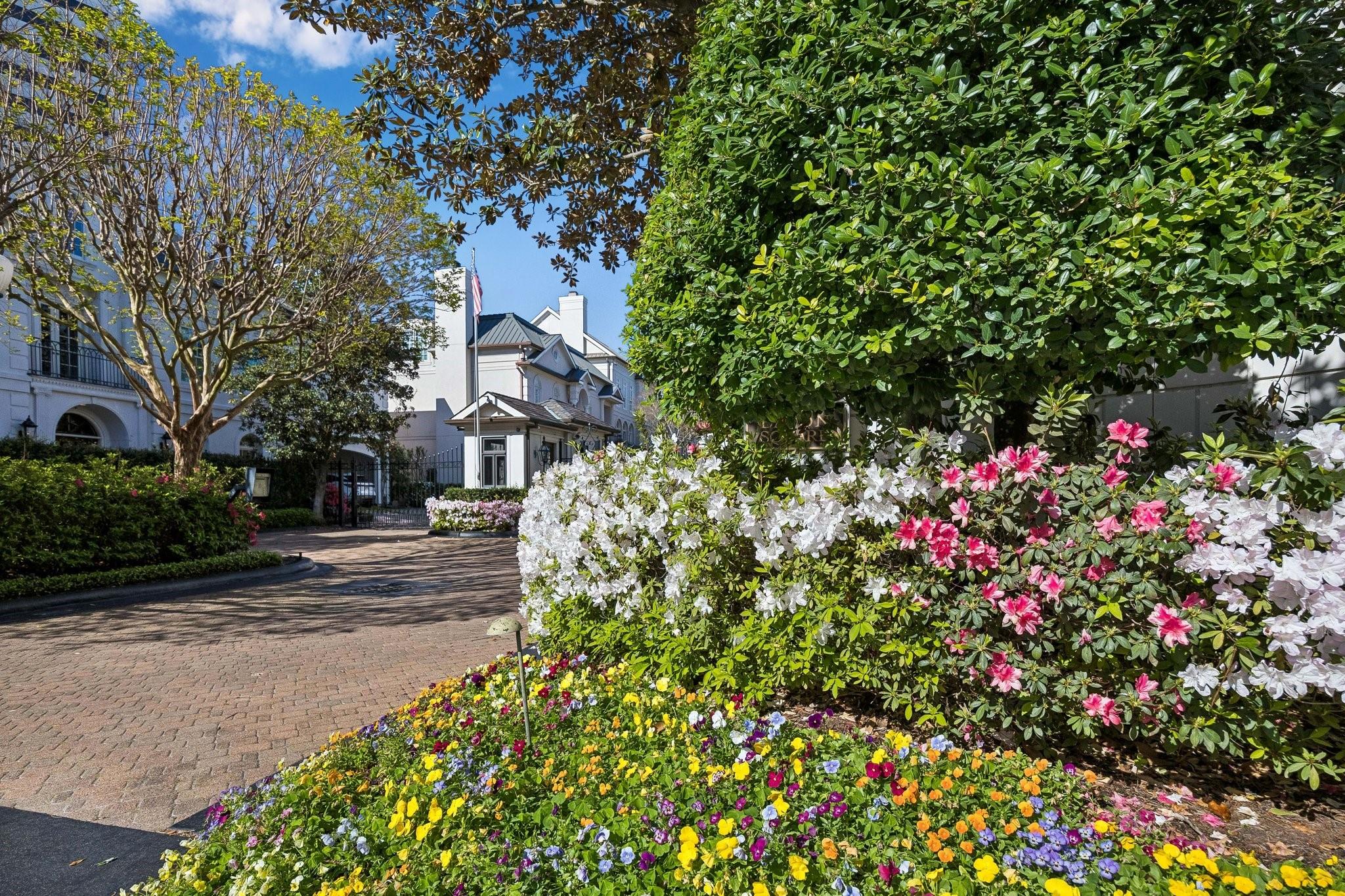 White homes behind a brick-paved entrance, framed by blooming azaleas and colorful flower beds.