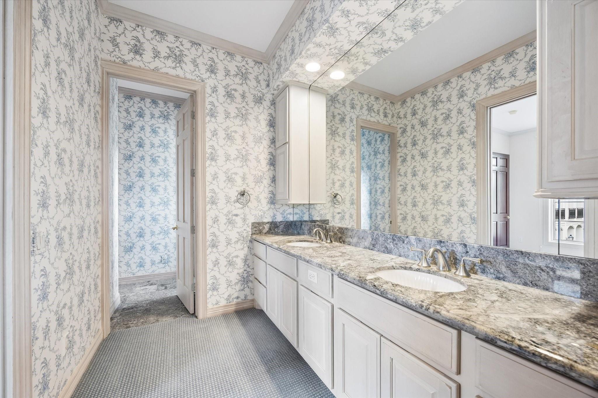 Bathroom with a double-sink vanity, stone countertop, large mirror, and blue-gray toile wallpaper.
