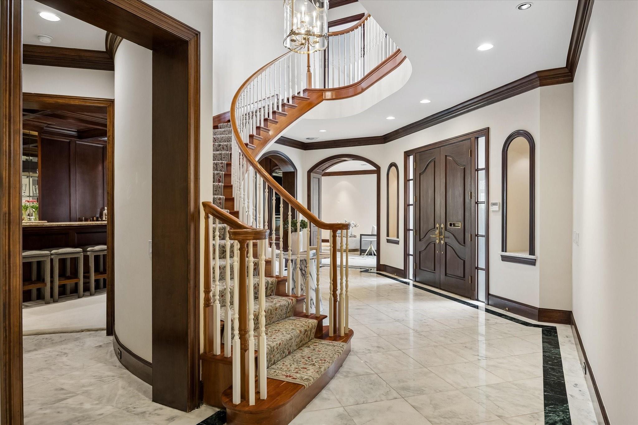 Foyer with a curved staircase, chandelier, marble tile floor, and dark wood double doors.