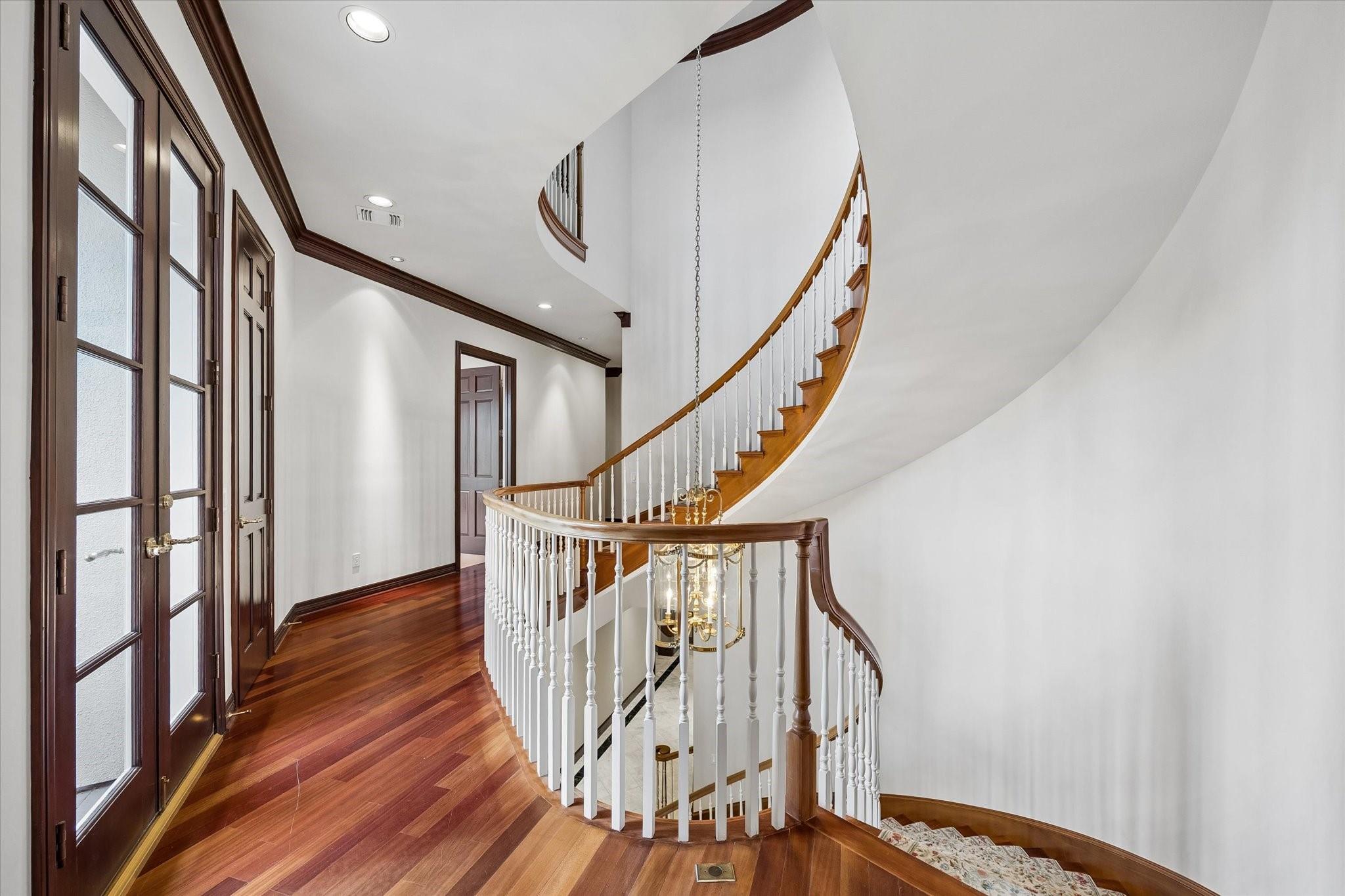 Upper landing with a sweeping curved staircase, white balusters, dark wood rail, and polished hardwood floors.
