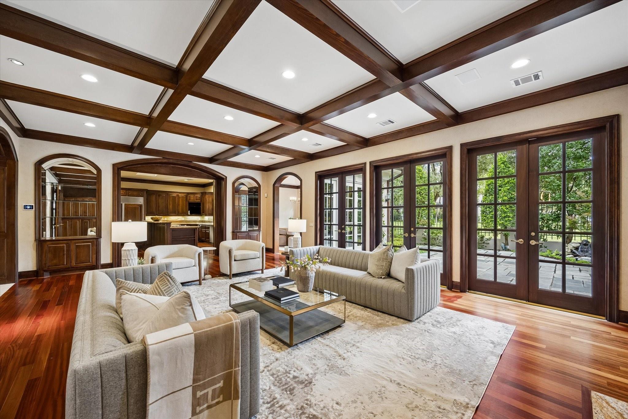 Living room with a dark wood coffered ceiling, neutral seating, hardwood floors, and French doors to a garden patio.