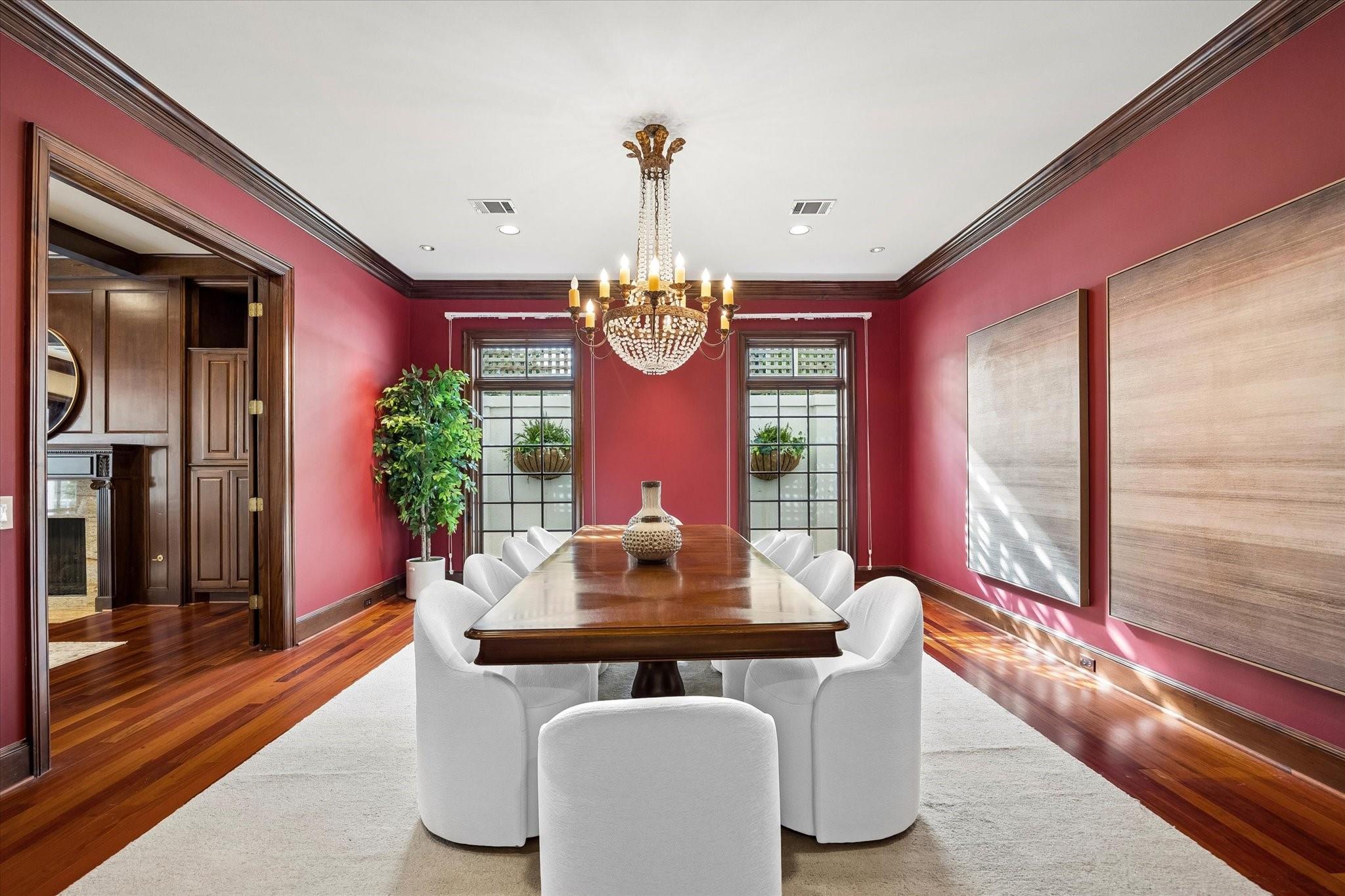 Dining room with red walls, a polished wood table, white chairs, and a crystal chandelier.