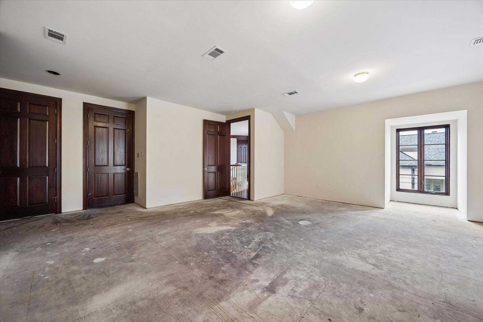 Unfinished empty room with dark wood doors, a rough floor, and a window.