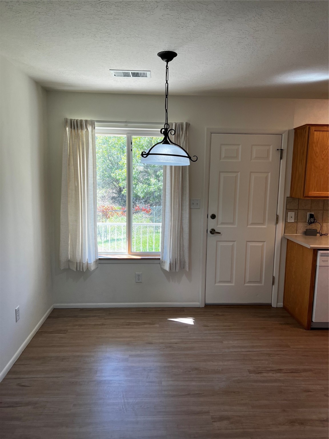 Empty dining area with wood-look flooring, a hanging light, and a curtained window.