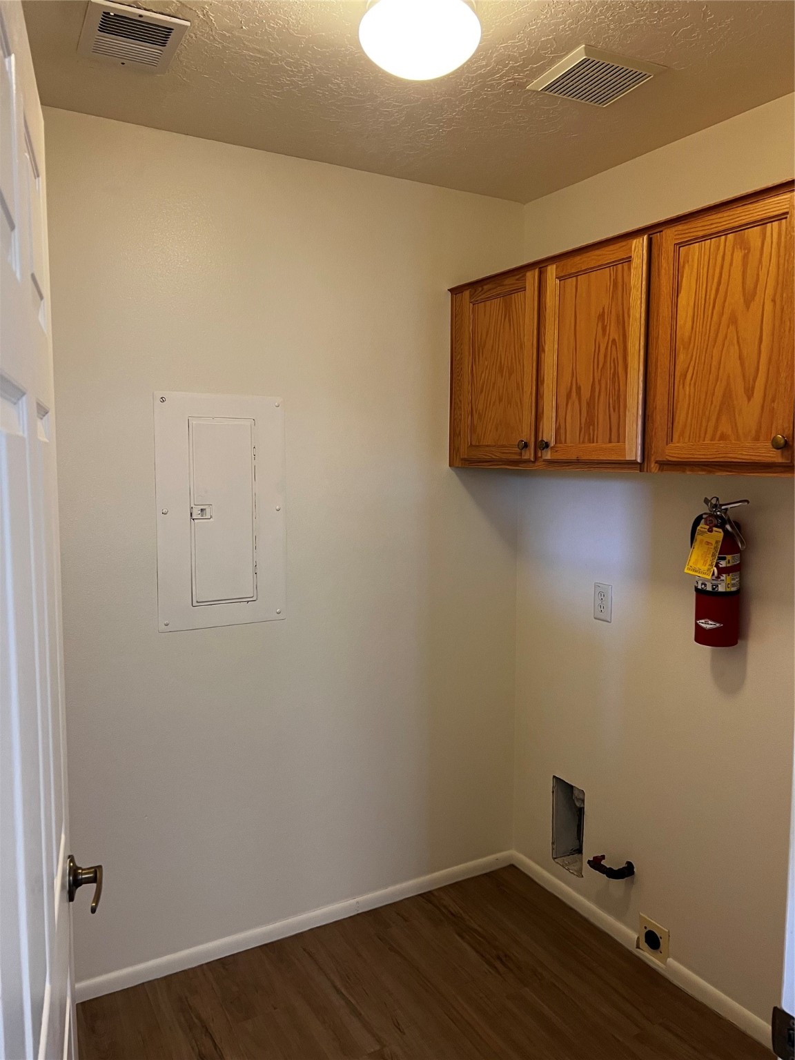 Vacant laundry room with oak cabinets, washer hookups, and wood-look flooring.