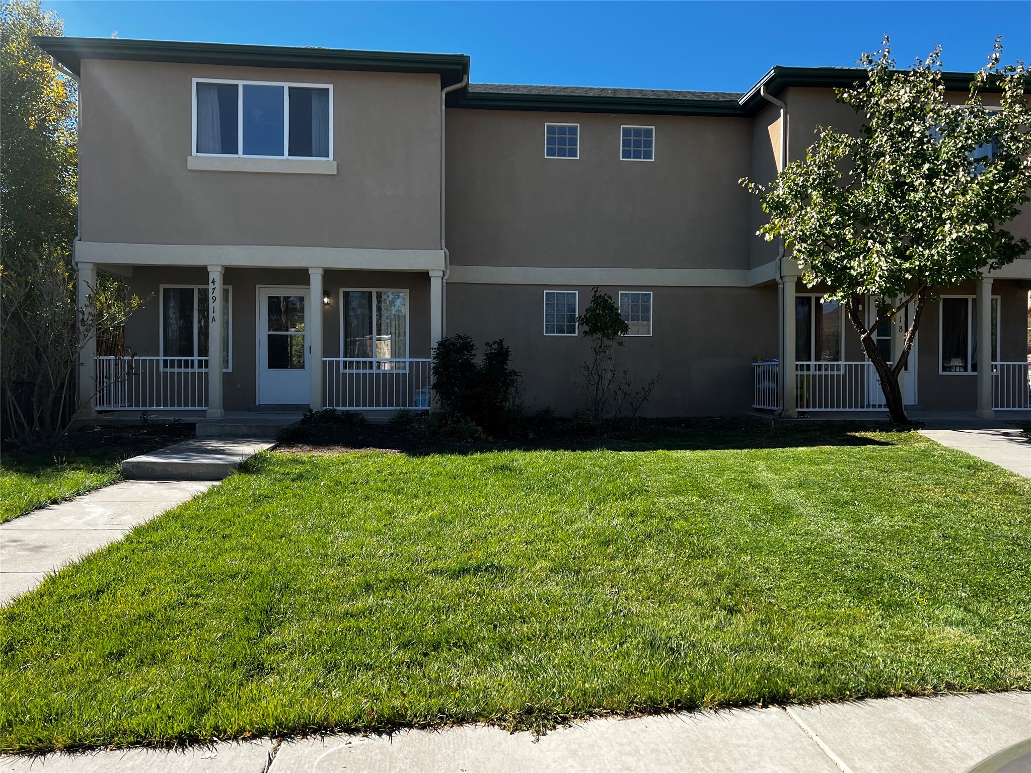 Two-story stucco duplex with separate covered entrances and a broad green lawn.