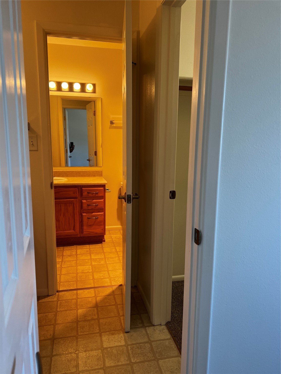 Bathroom with a wood vanity, mirror, bright vanity lights, and square tile flooring.