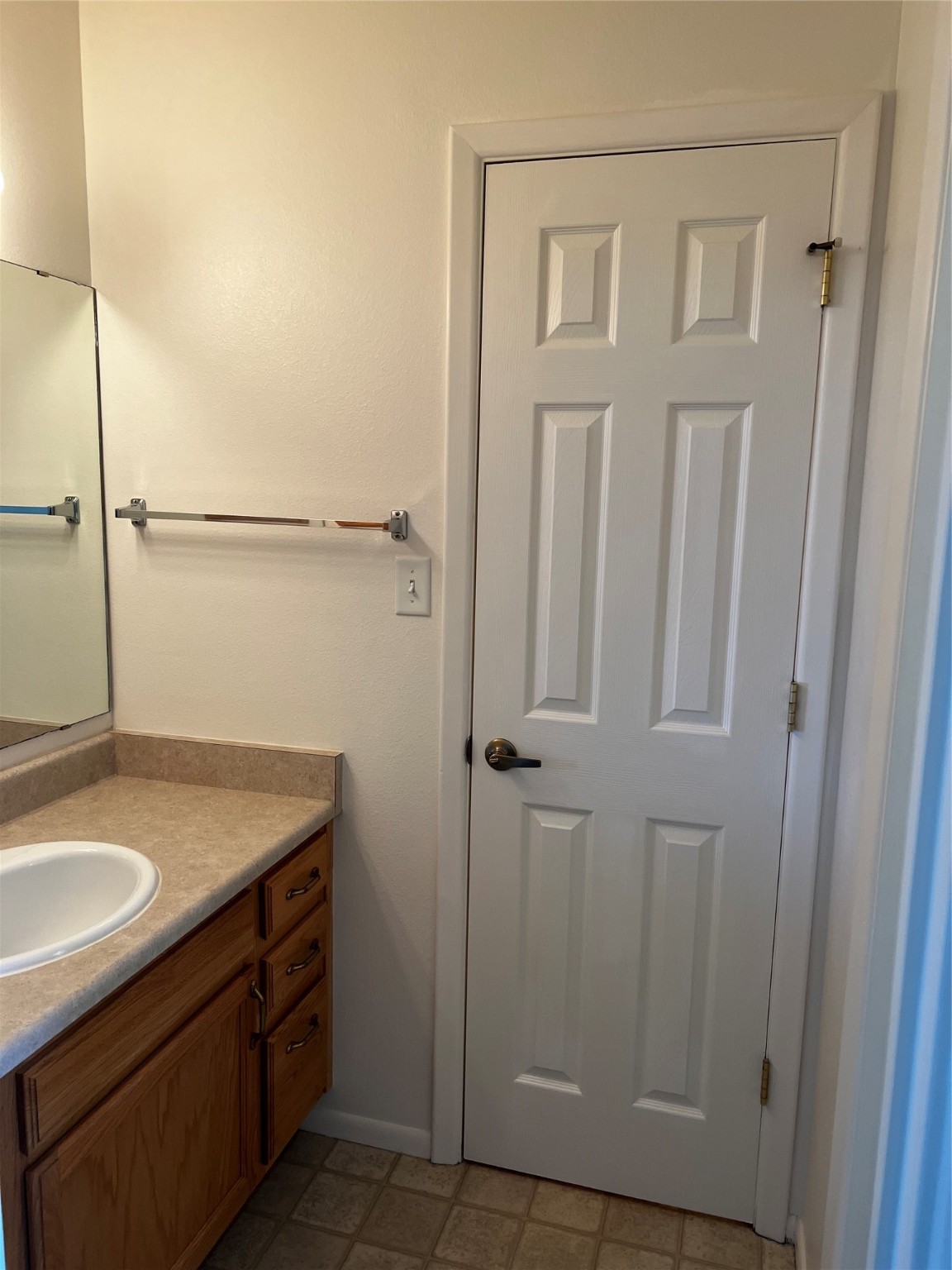 Bathroom vanity with a beige countertop and sink beside a white paneled door.