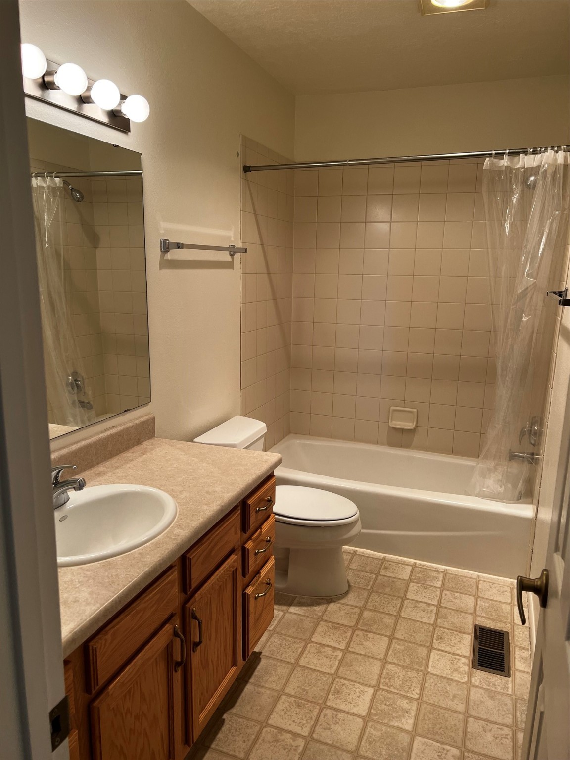 Bathroom with a tiled tub and shower, wooden vanity, sink, and toilet.