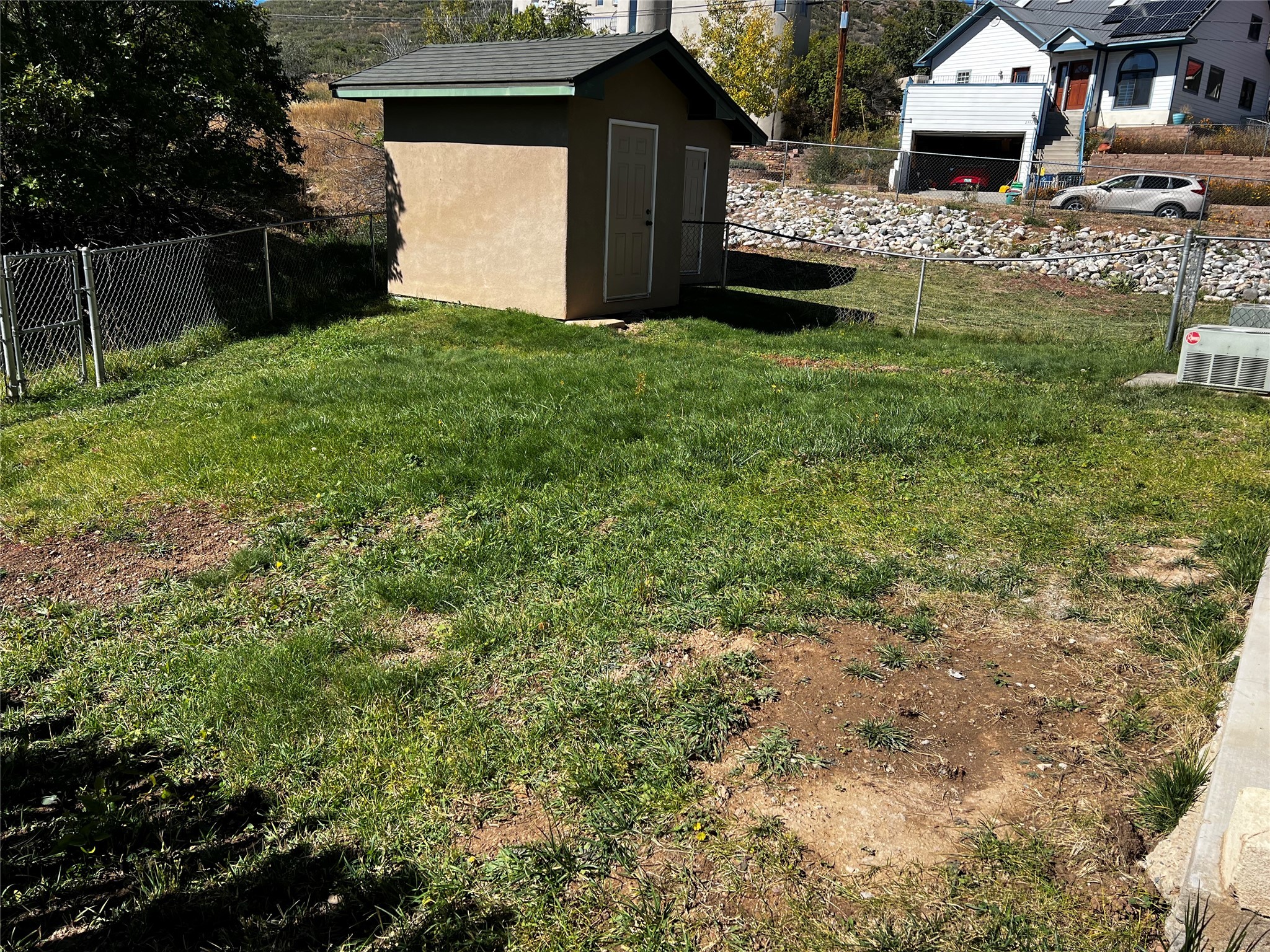 Fenced grassy yard with a tan storage shed and patches of bare soil.