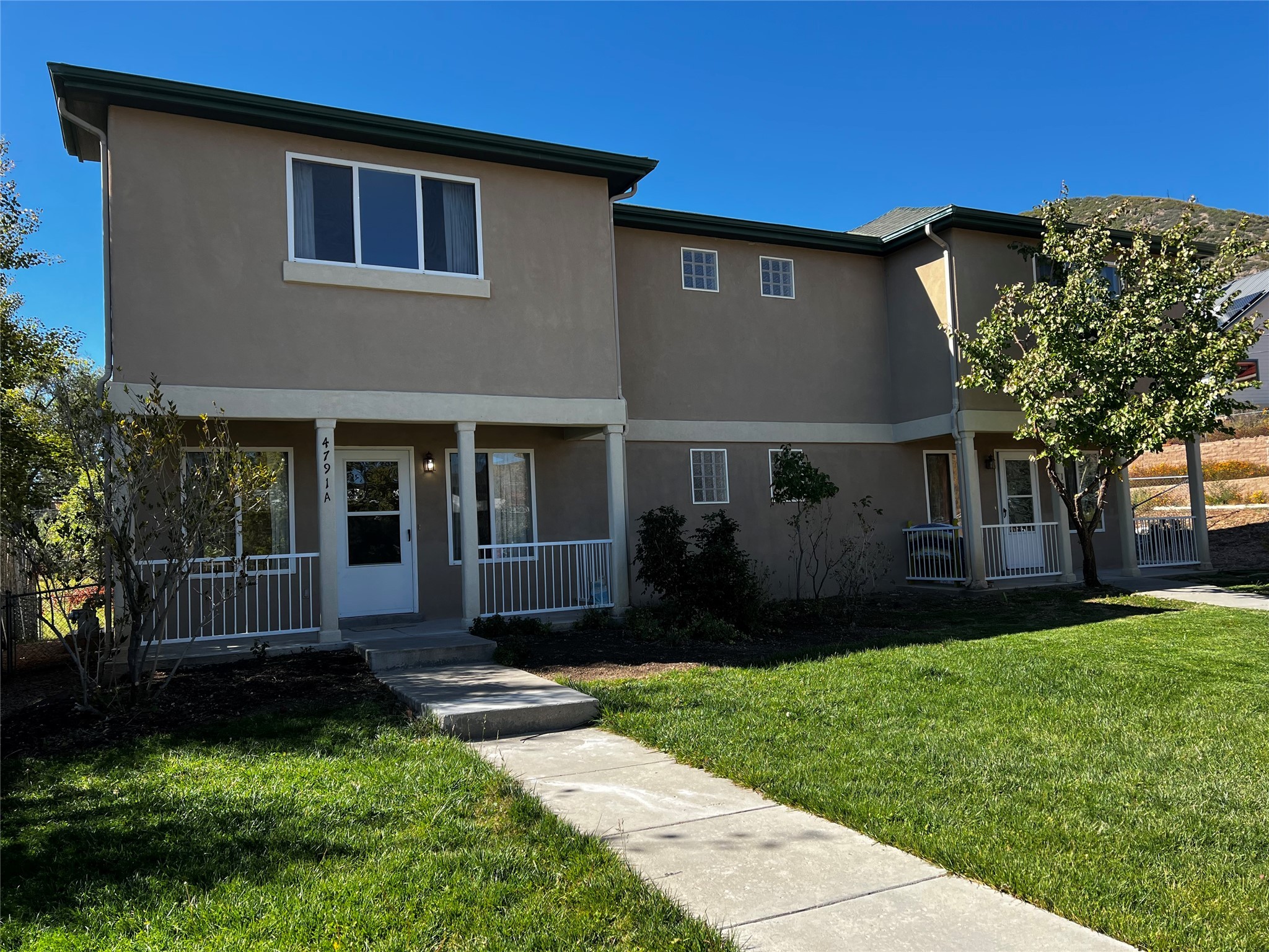 Two-story beige home with adjoining porches, white railings, and a lawn.