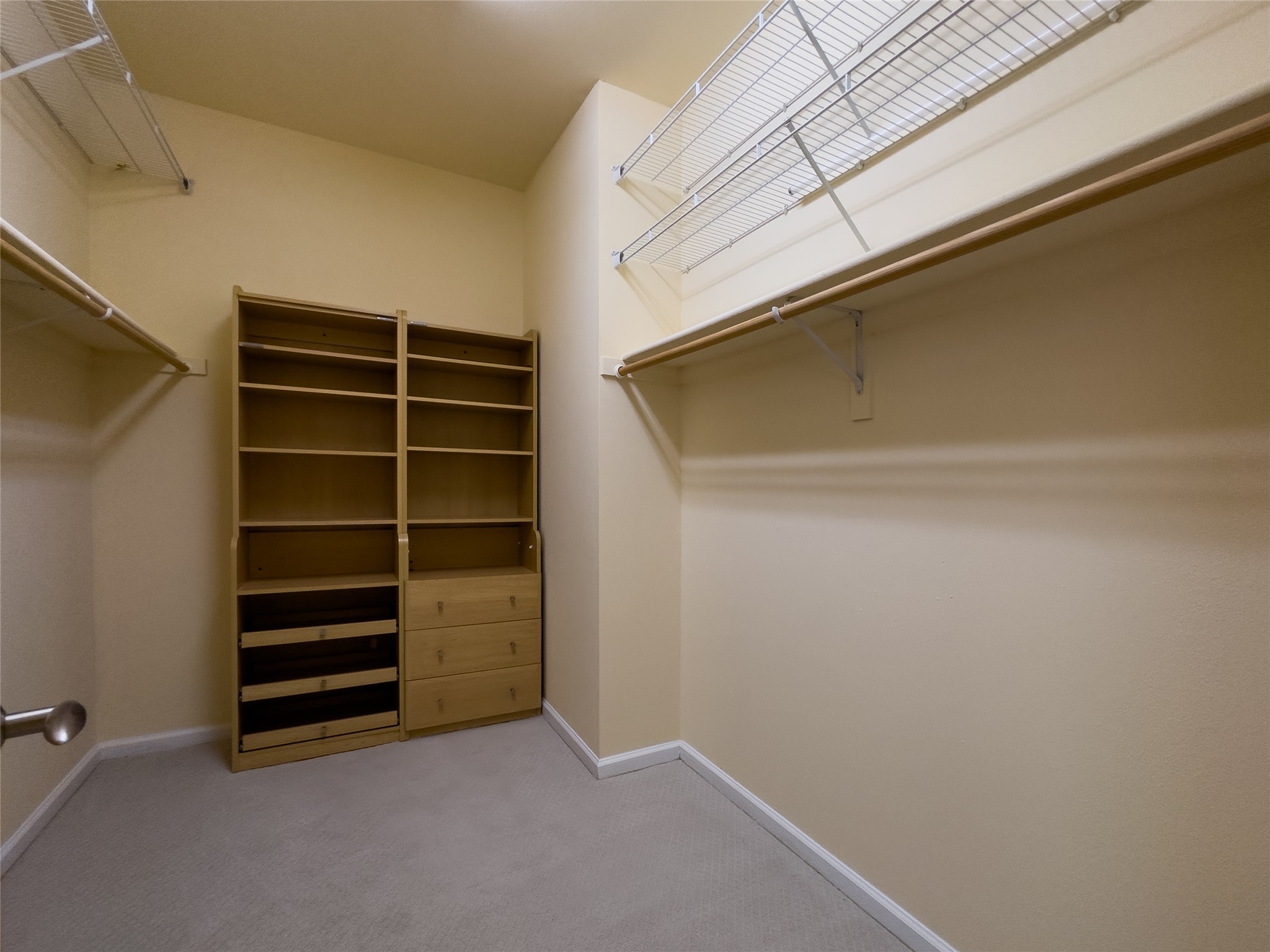 Walk-in closet with extensive hanging rods, wire shelving, and a wooden drawer-and-shelf organizer.