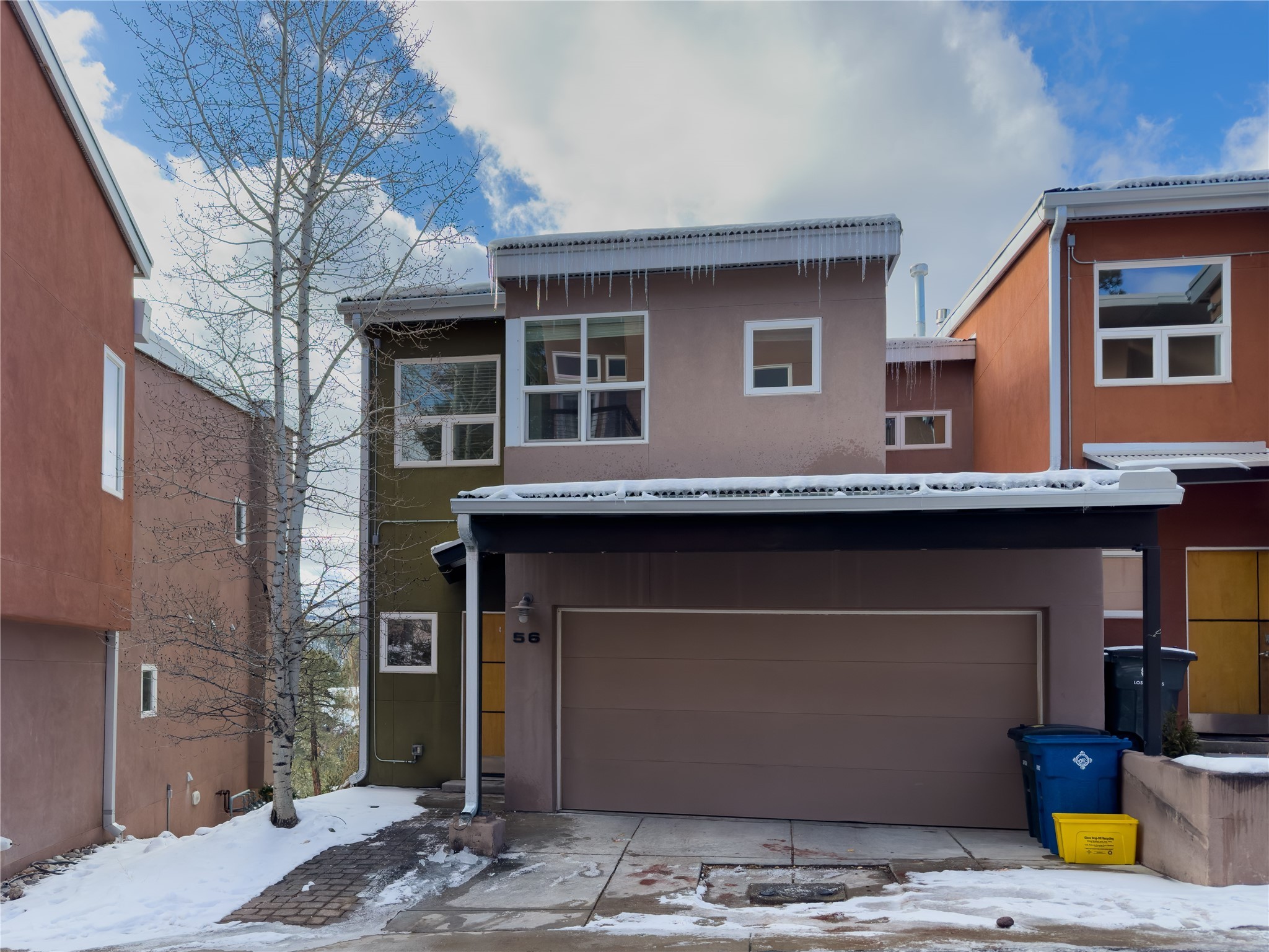 Modern multi-level home with a double garage, snowy driveway, and icicles hanging from the roof.