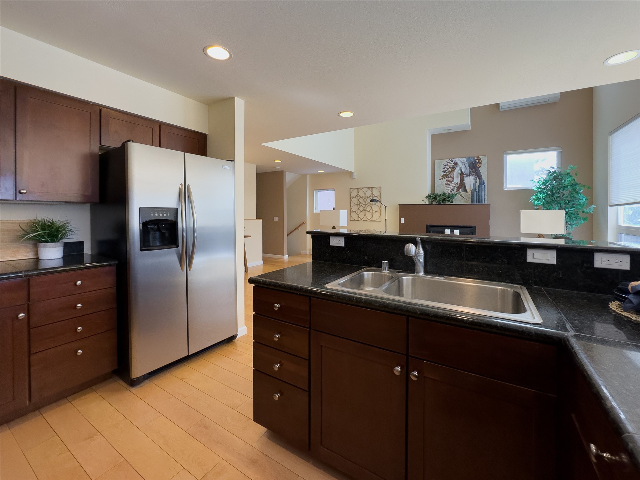 Kitchen with dark wood cabinets, black granite counters, stainless steel refrigerator, and a large sink peninsula.