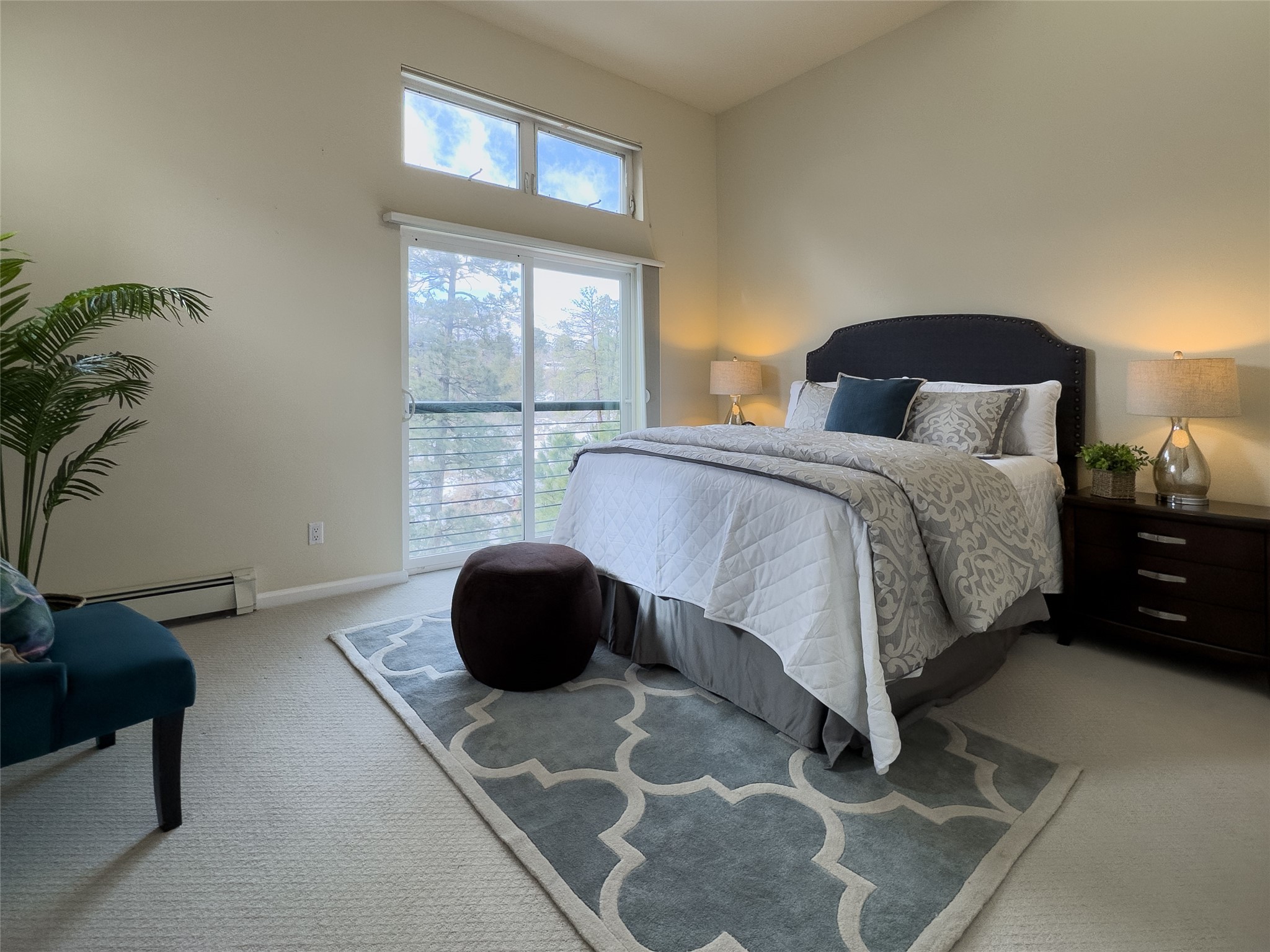 Staged bedroom with a large bed beside a sliding glass door overlooking trees.