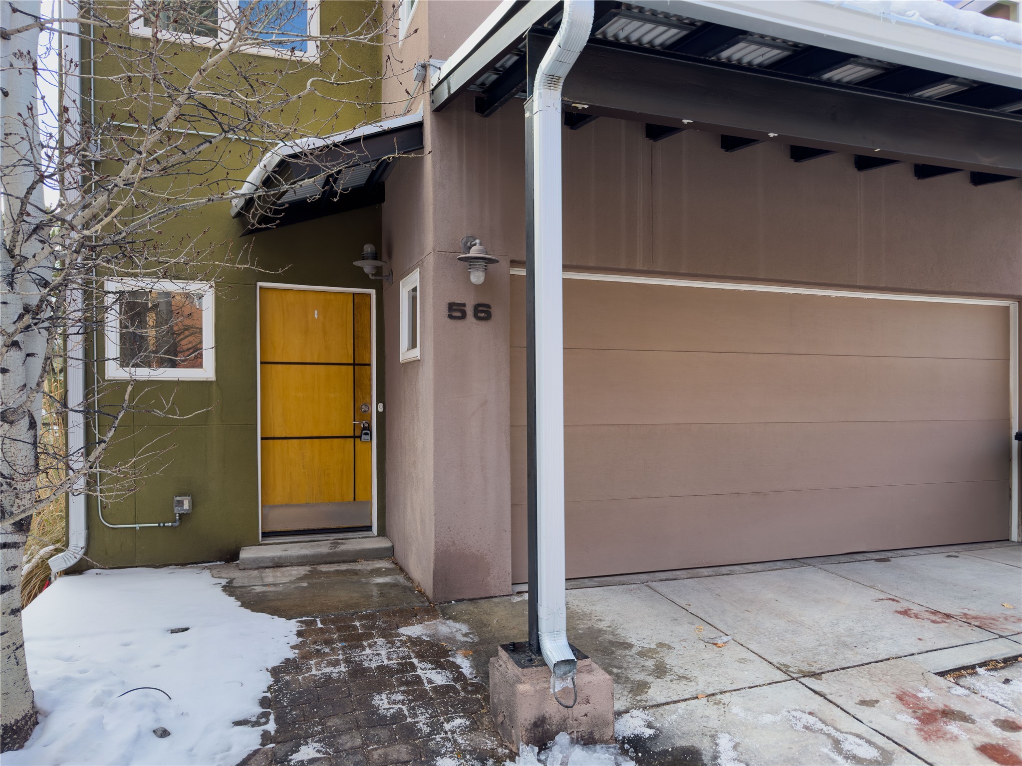 Home entrance with a yellow door, attached garage, and snow along the walkway.
