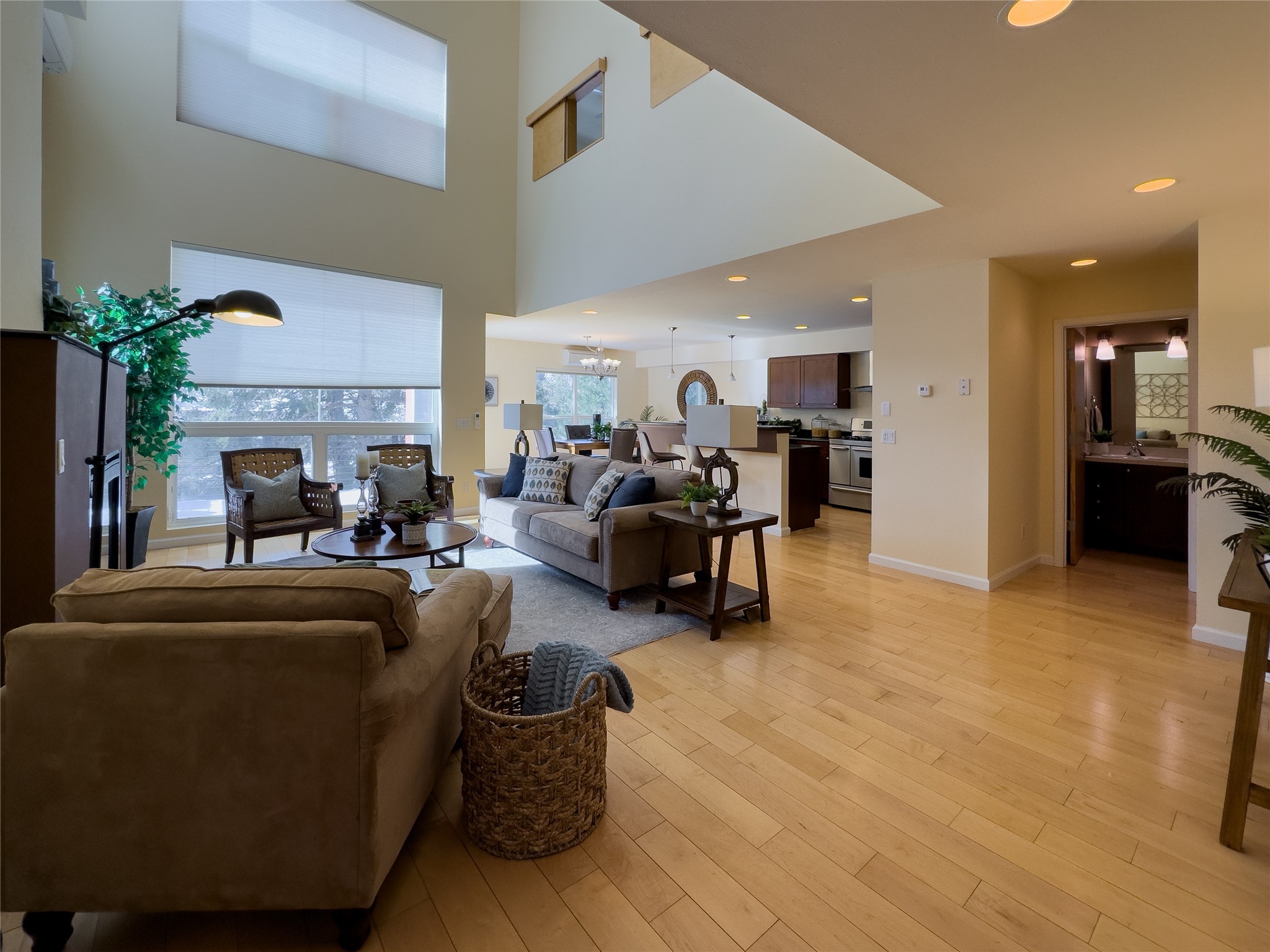 Open-plan living room with vaulted ceiling, tall windows, and wood floors.