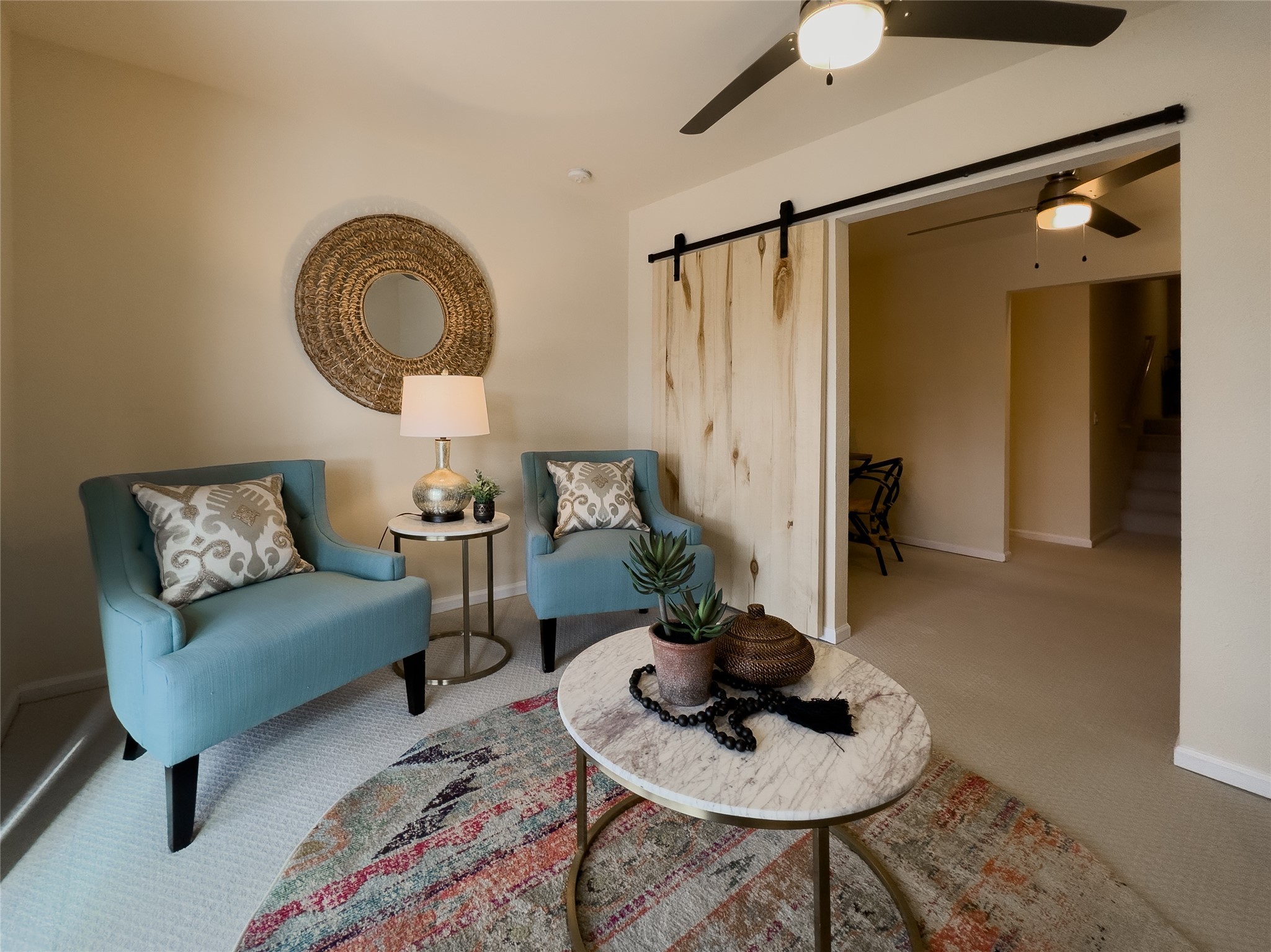 Staged sitting area with teal armchairs, a marble-top coffee table, and a sliding wood barn door.