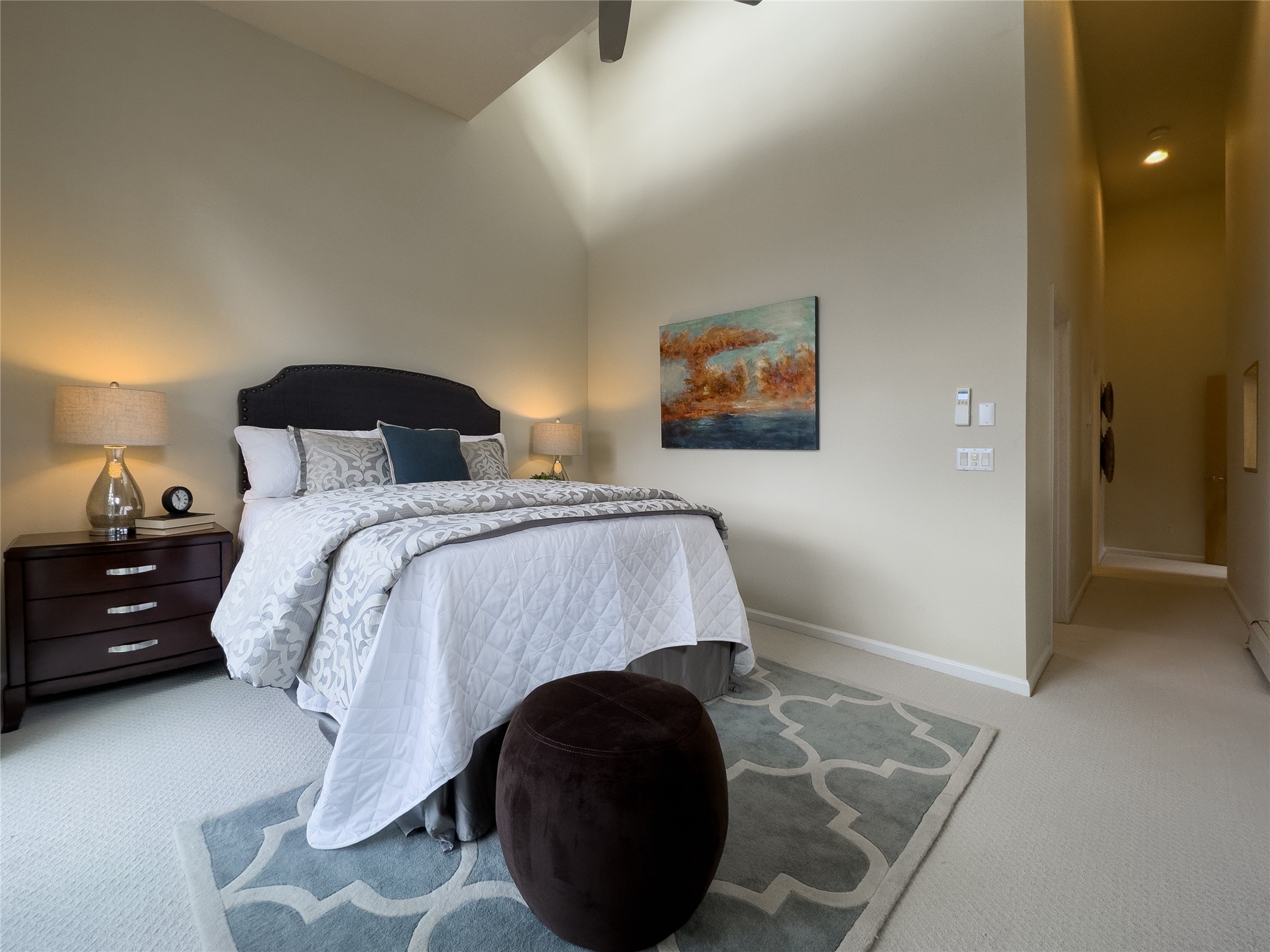 Furnished bedroom with a king-size bed, patterned bedding, gray rug, and abstract wall art.
