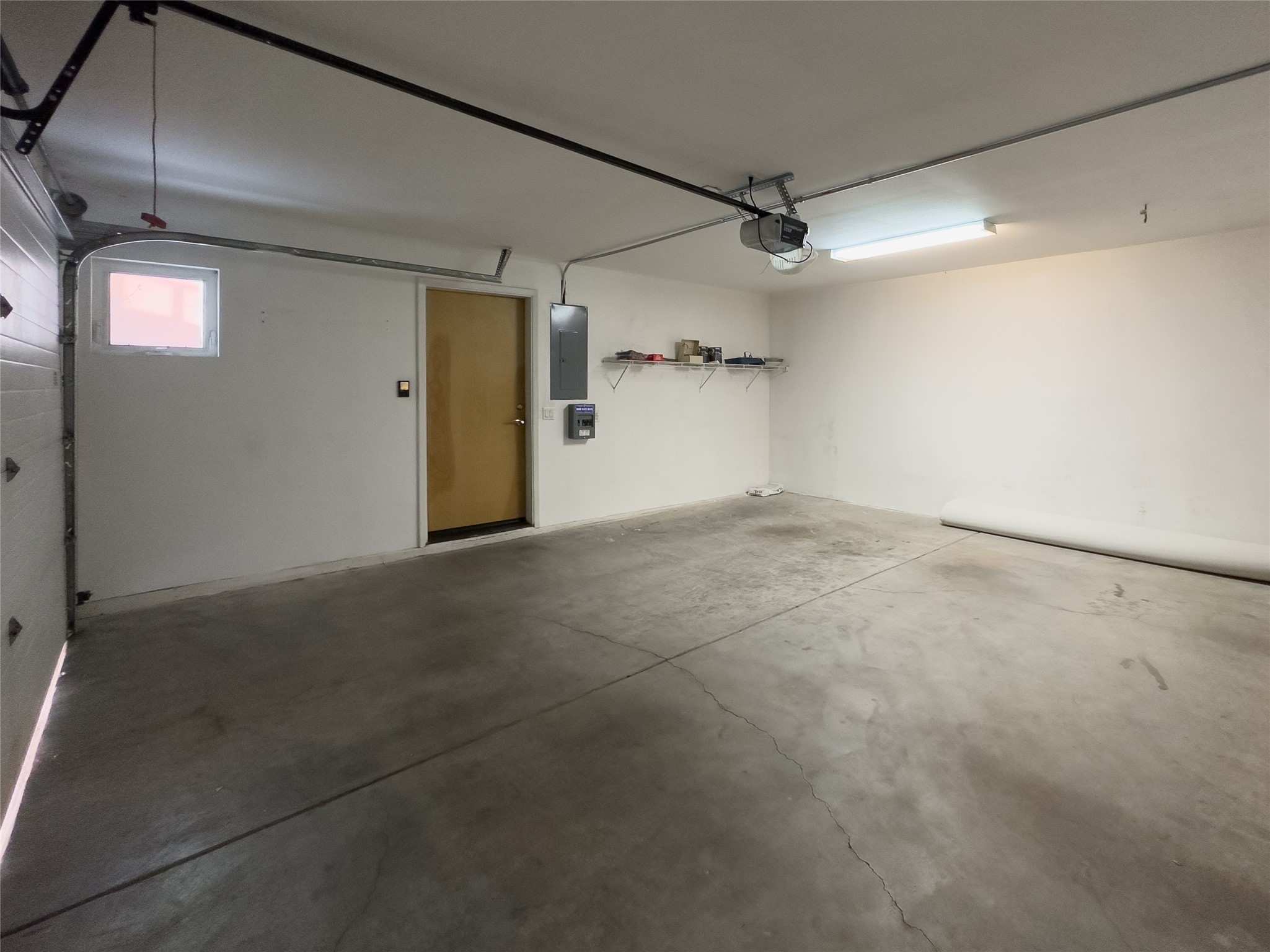 Mostly empty garage with a concrete floor, overhead door, high window, and side-entry door.