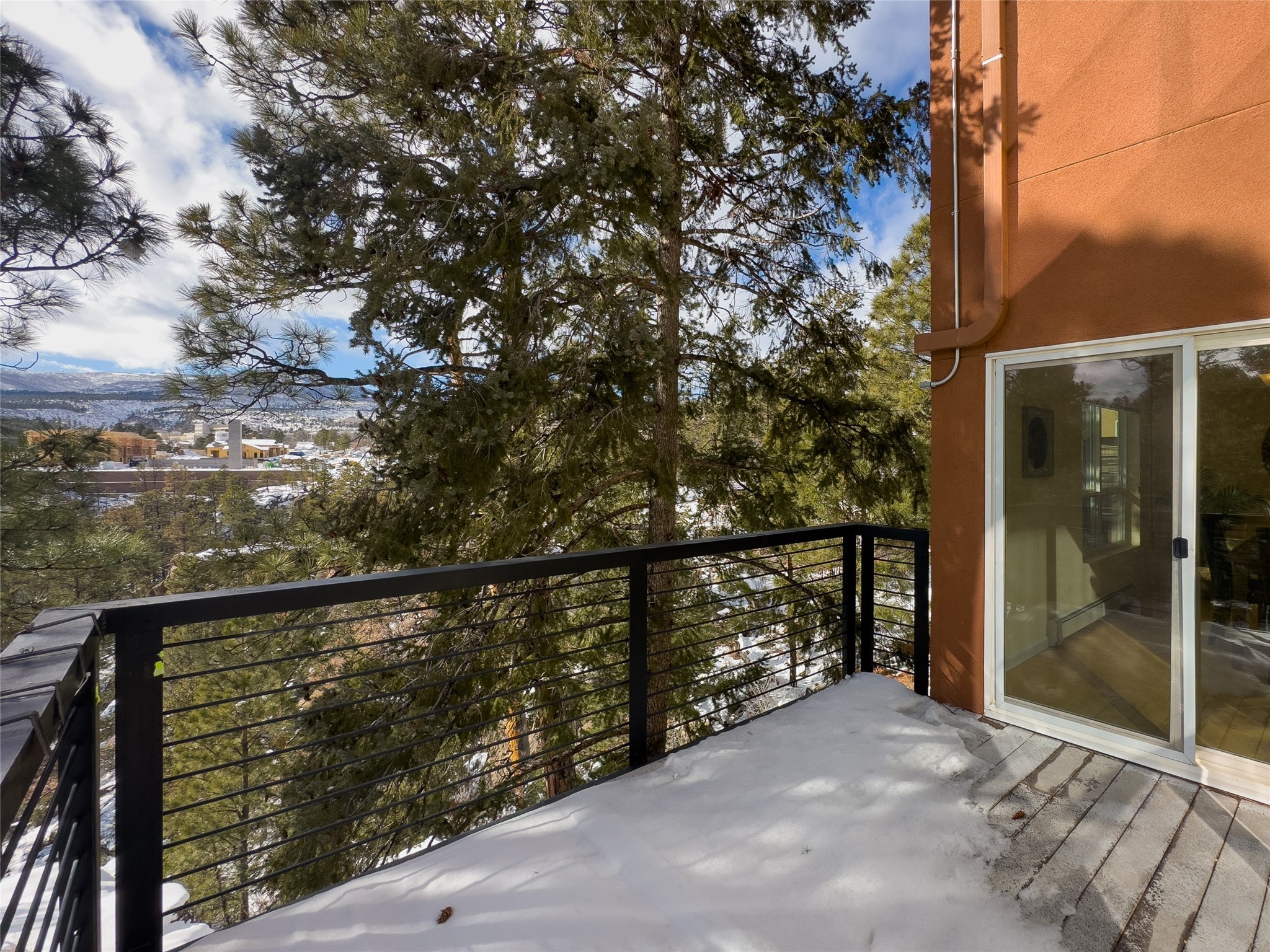 Snowy balcony overlooking evergreen trees, a town, and distant mountains.