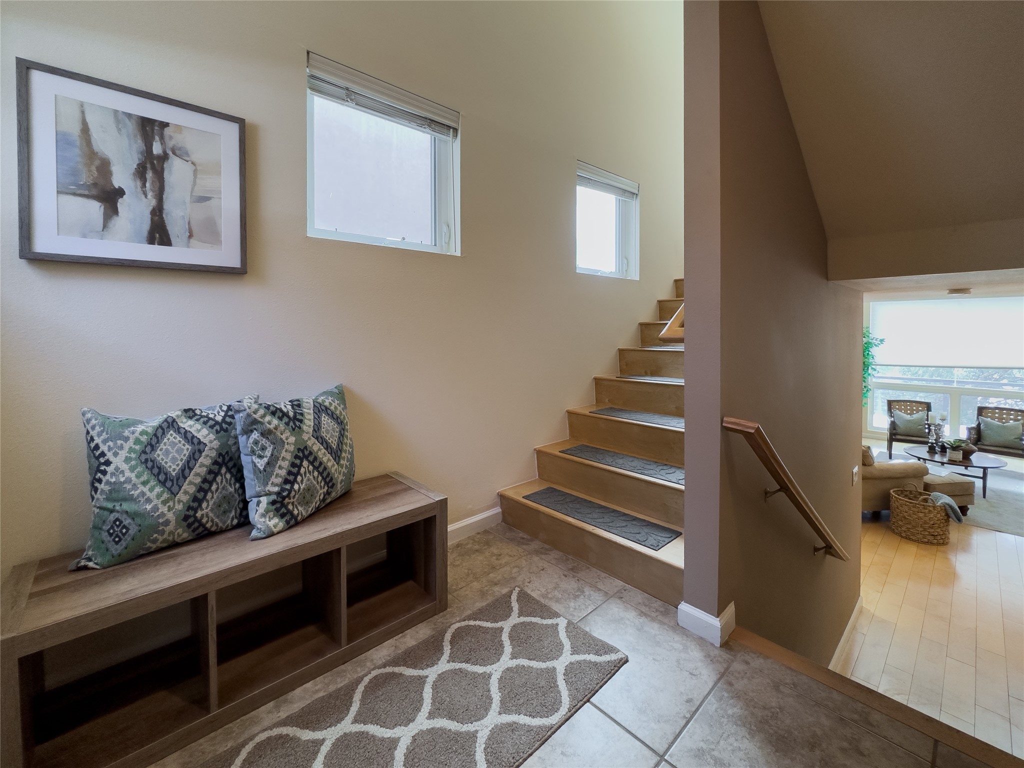 Furnished entryway with a cushioned bench, tiled floor, and staircase beside a glimpse of the living area.