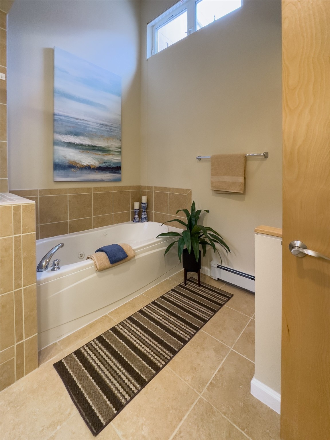 Bathroom with a built-in jetted tub, tan tile, and striped runner.