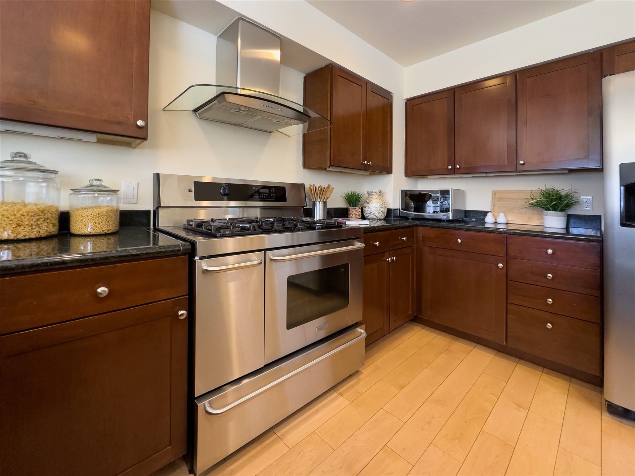 Kitchen with dark wood cabinets, black counters, and a stainless steel gas range beneath a glass hood.