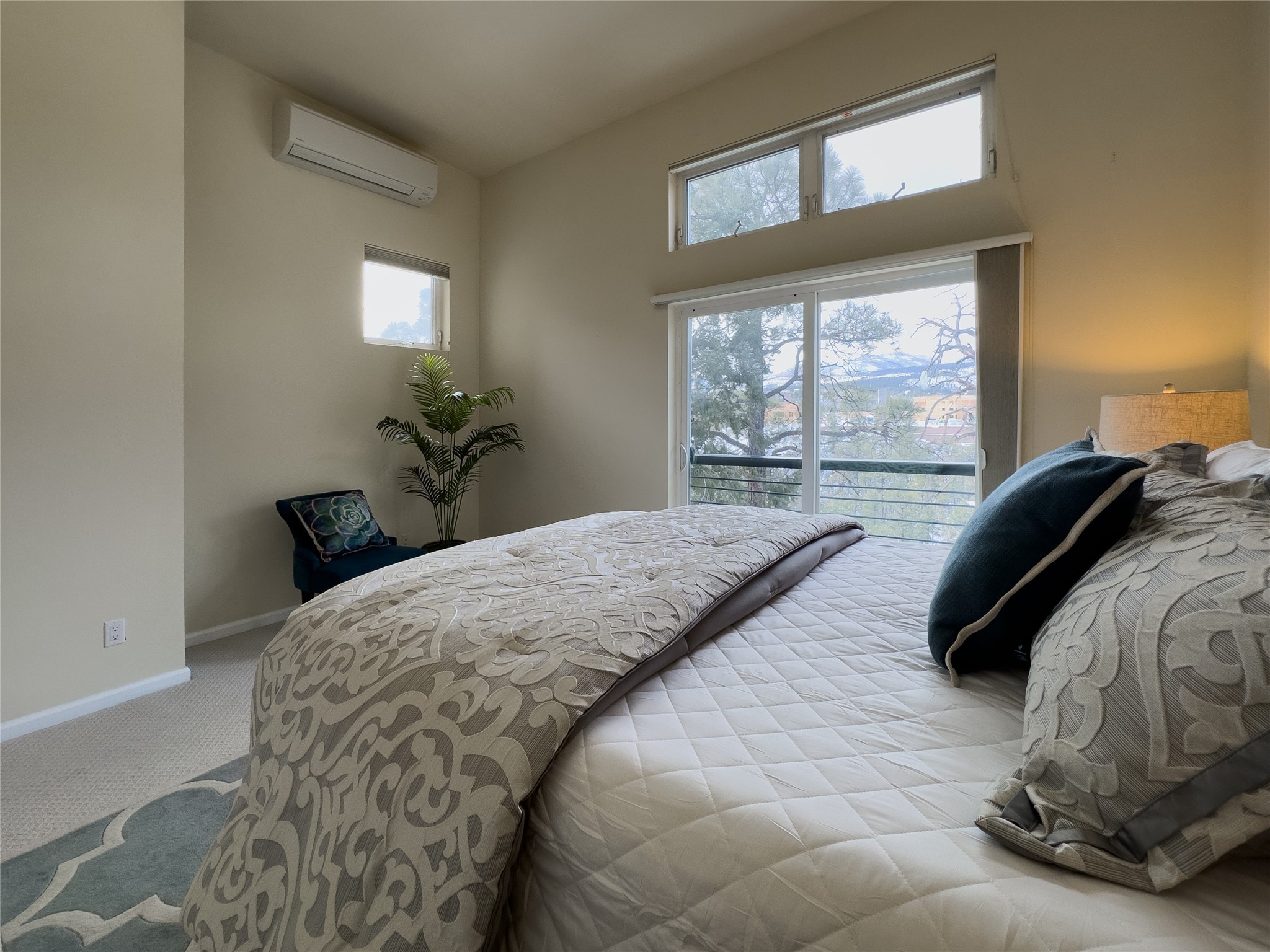 Furnished bedroom with patterned bedding and a sliding glass door overlooking trees.