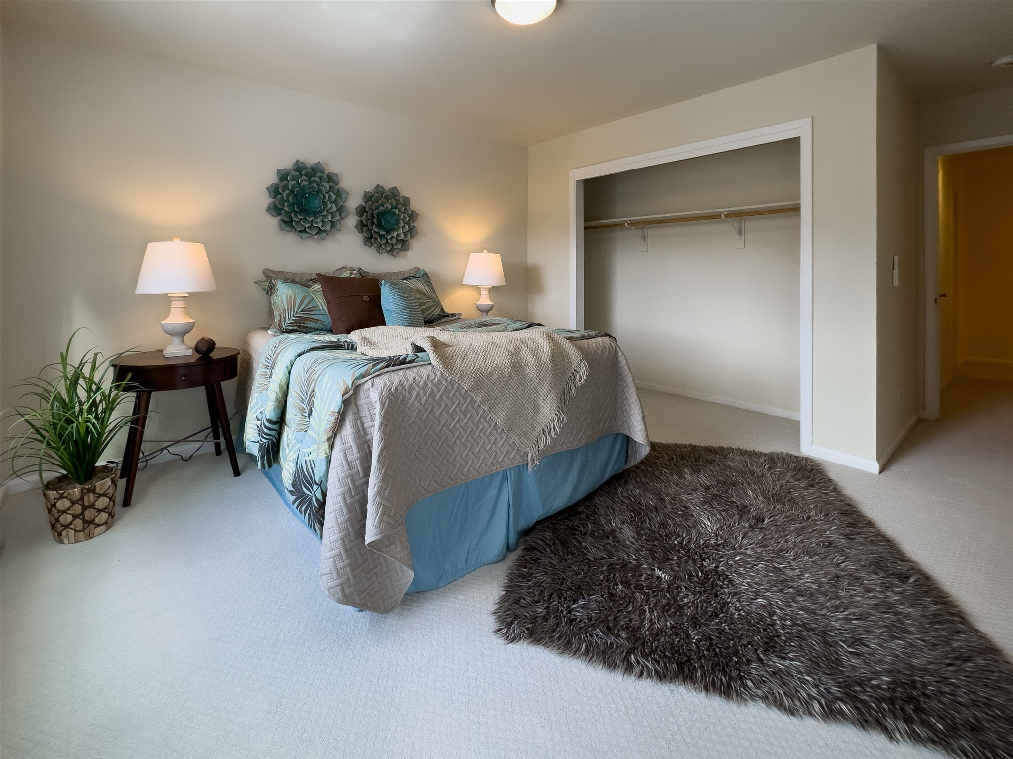 Staged bedroom with blue patterned bedding, a large dark shag rug, and an open closet.