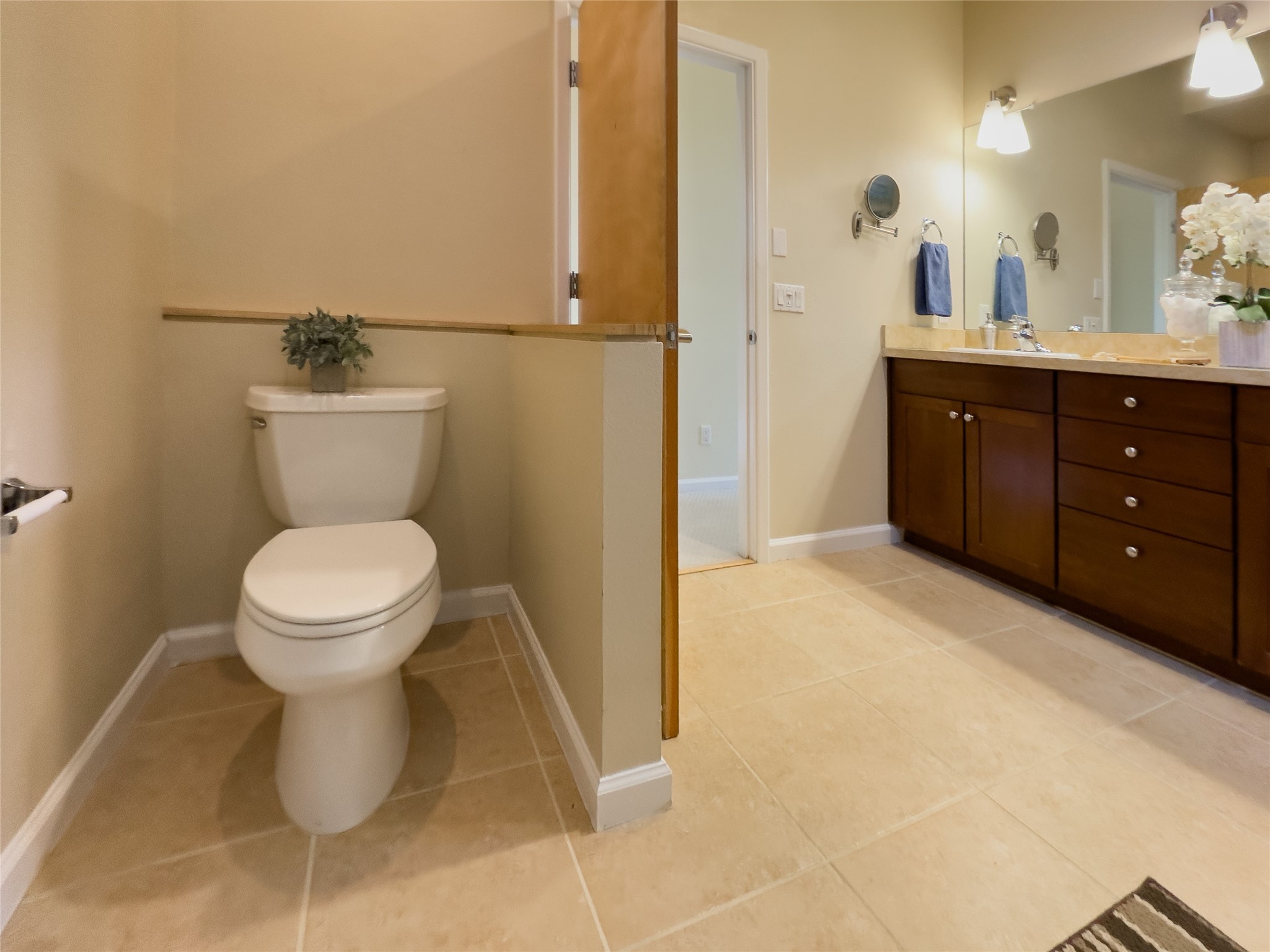 Bathroom with a separate toilet alcove and a long dark wood vanity beneath a large mirror.