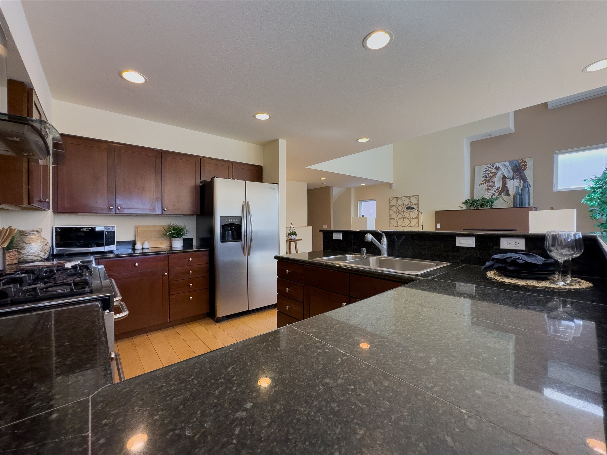Kitchen with dark wood cabinets, granite counters, a large island sink, and stainless steel appliances.