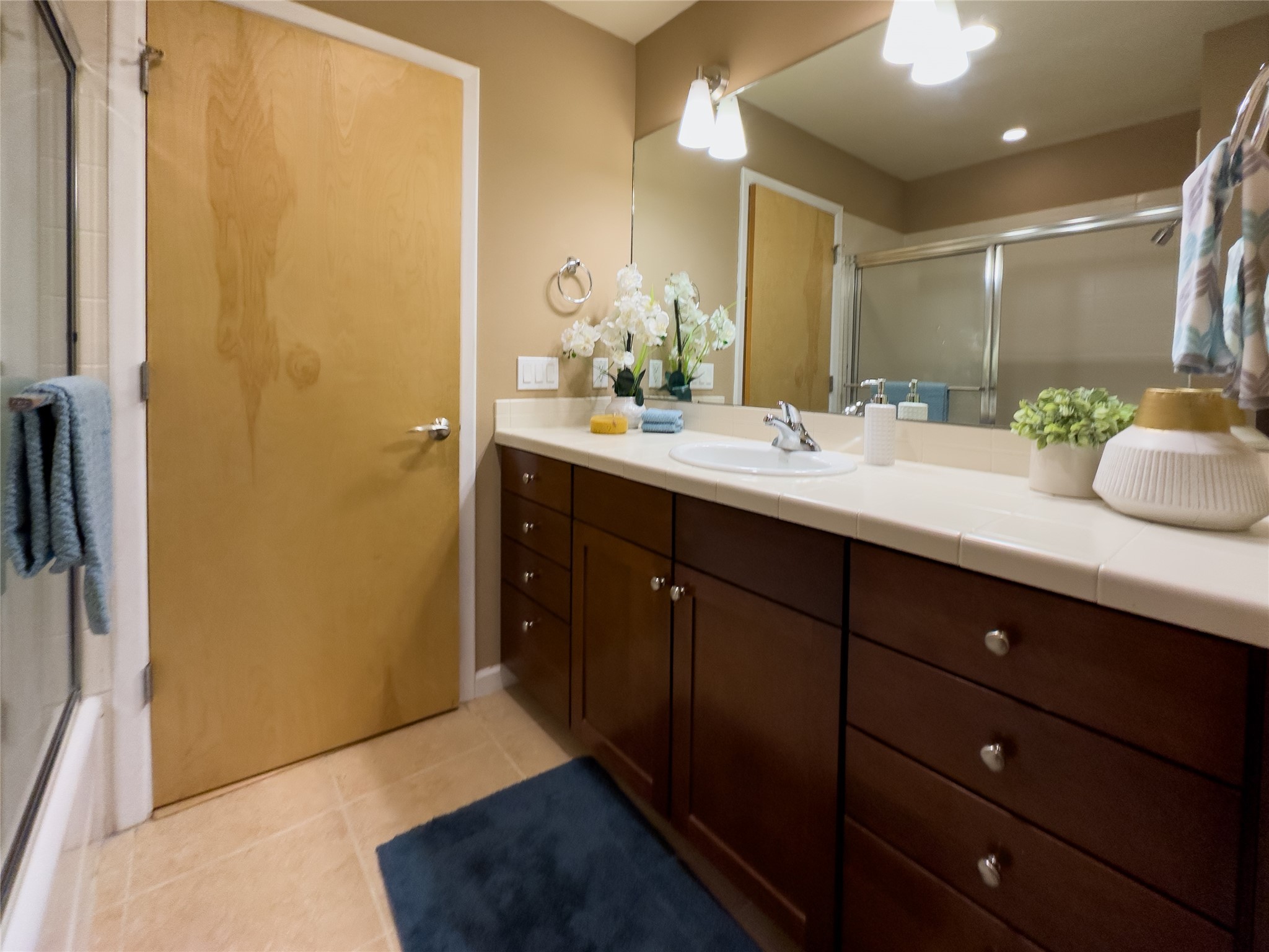 Bathroom with a long dark wood vanity, white countertop, large mirror, and glass-enclosed shower.