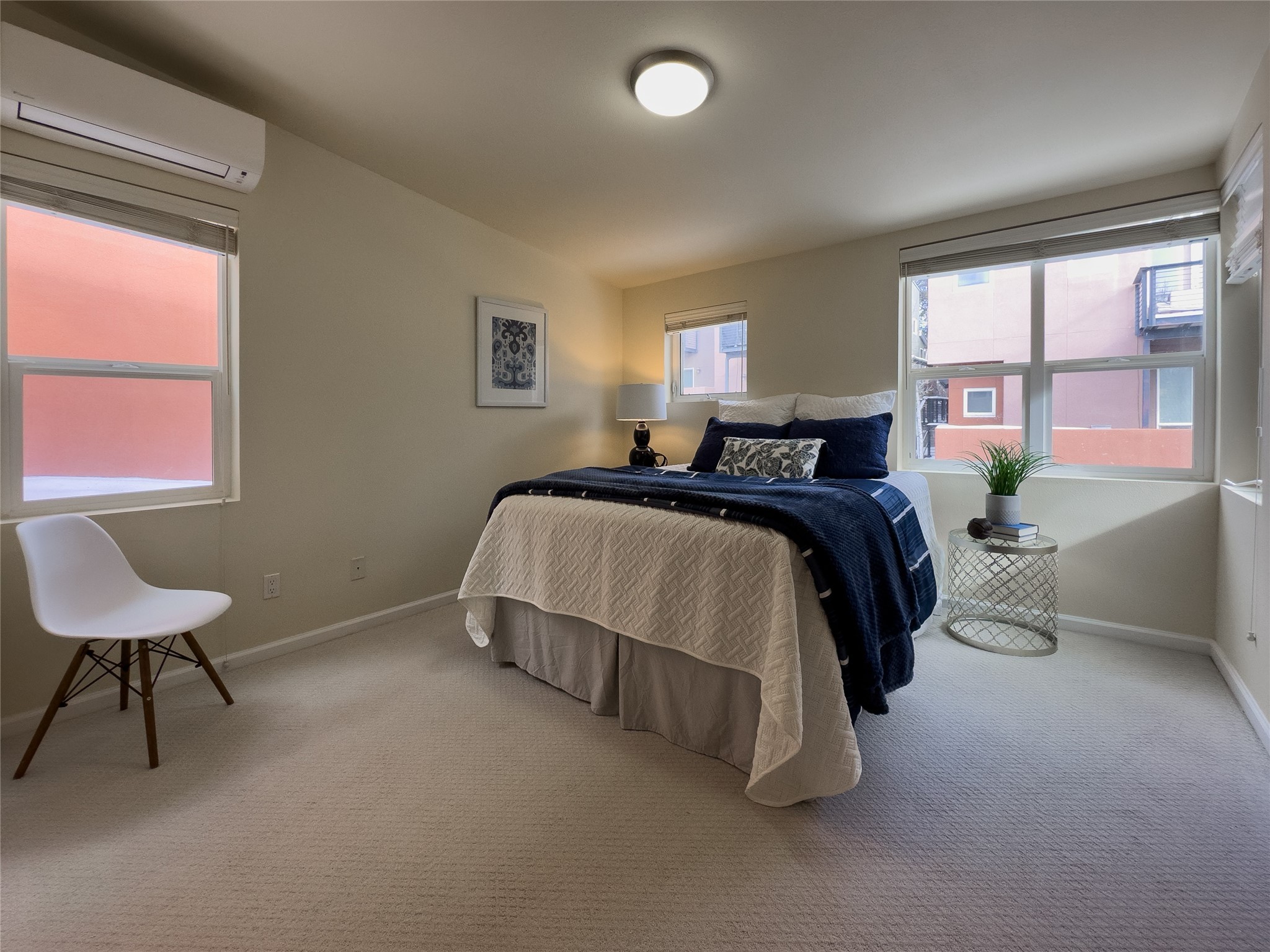 Furnished bedroom with a navy-and-white bed, beige carpet, and windows on three walls.
