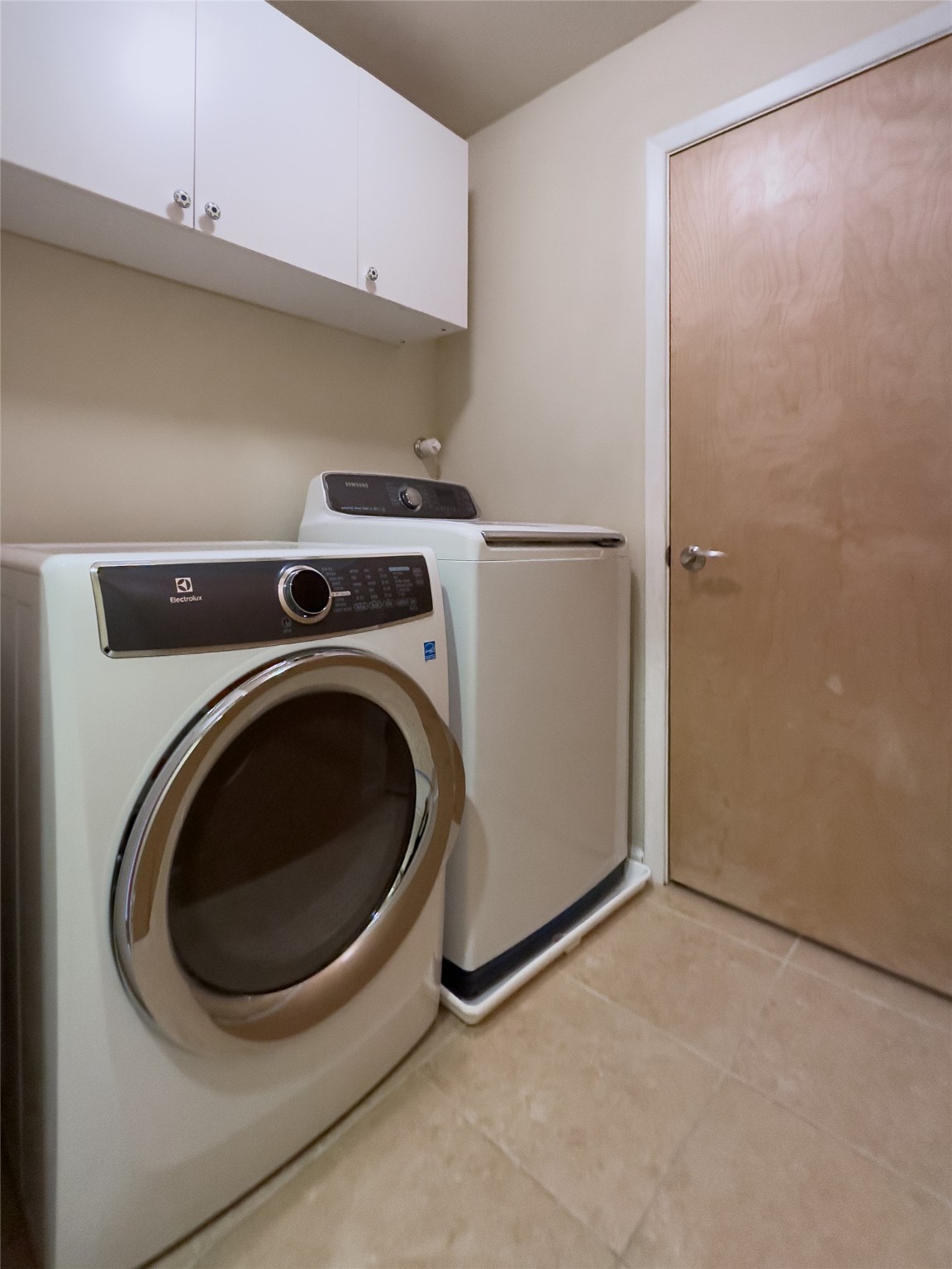 Laundry room with Electrolux dryer, Samsung washer, overhead cabinets, and beige tile floor.