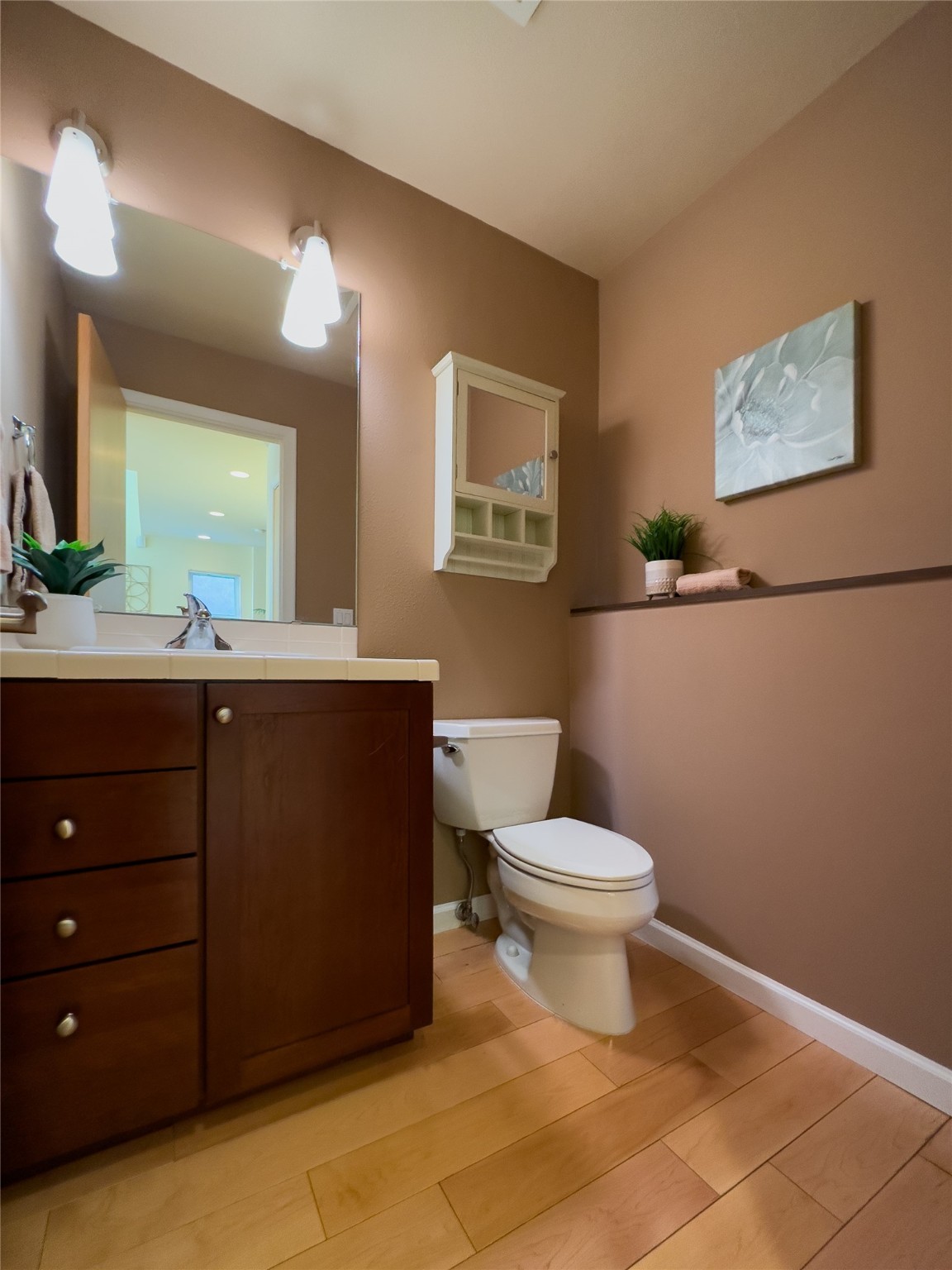 Bathroom with dark wood vanity, white toilet, and warm wood flooring.