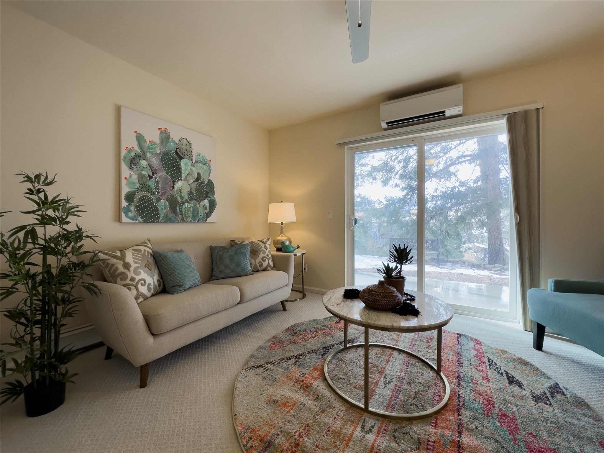Furnished living room with cactus artwork, a round coffee table, and sliding doors overlooking trees.