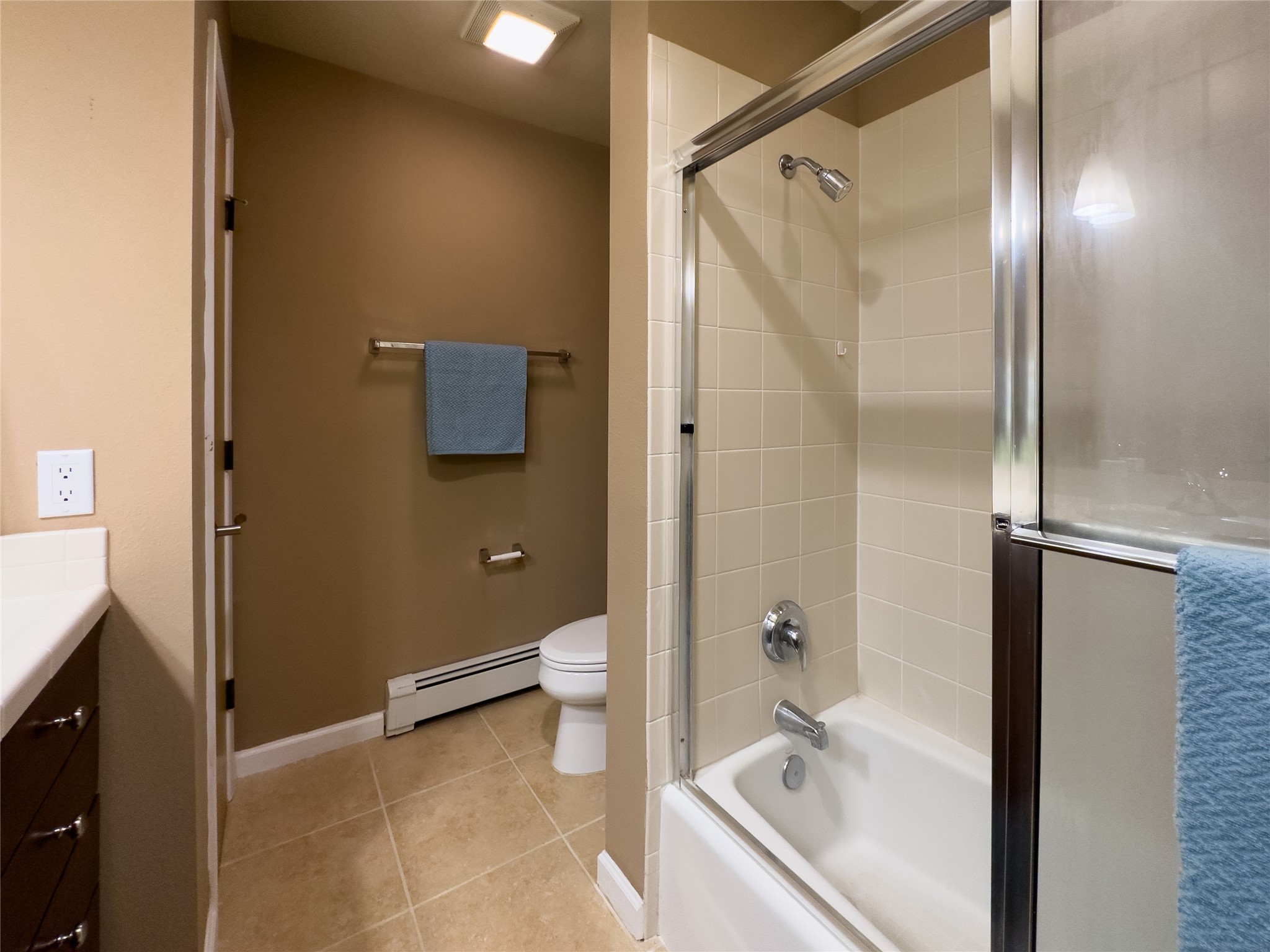 Bathroom with a glass-enclosed tub, cream tile, toilet, and dark wood vanity.