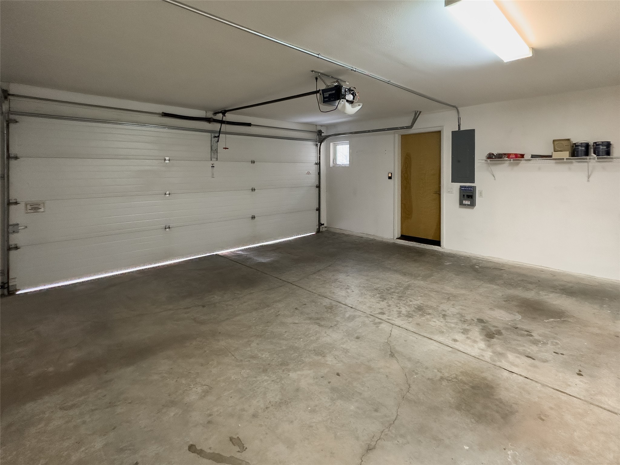 Empty garage with a closed overhead door, concrete floor, and side entry door.